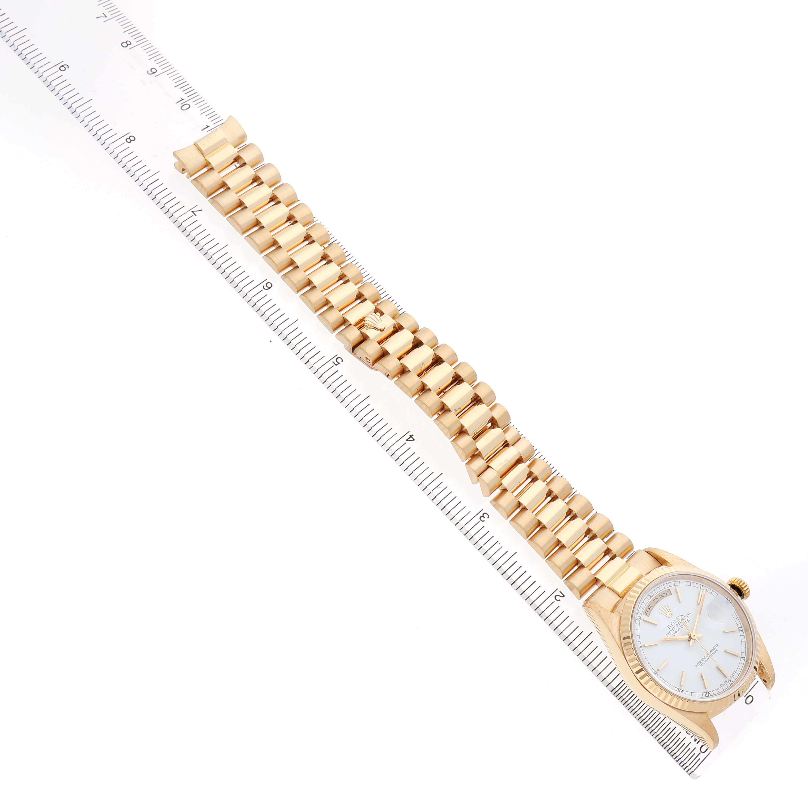 The Rolex President 18238 Men's Yellow Gold White Dial model watch is shown from an overhead angle, displaying its bracelet and dial alongside a ruler for scale.