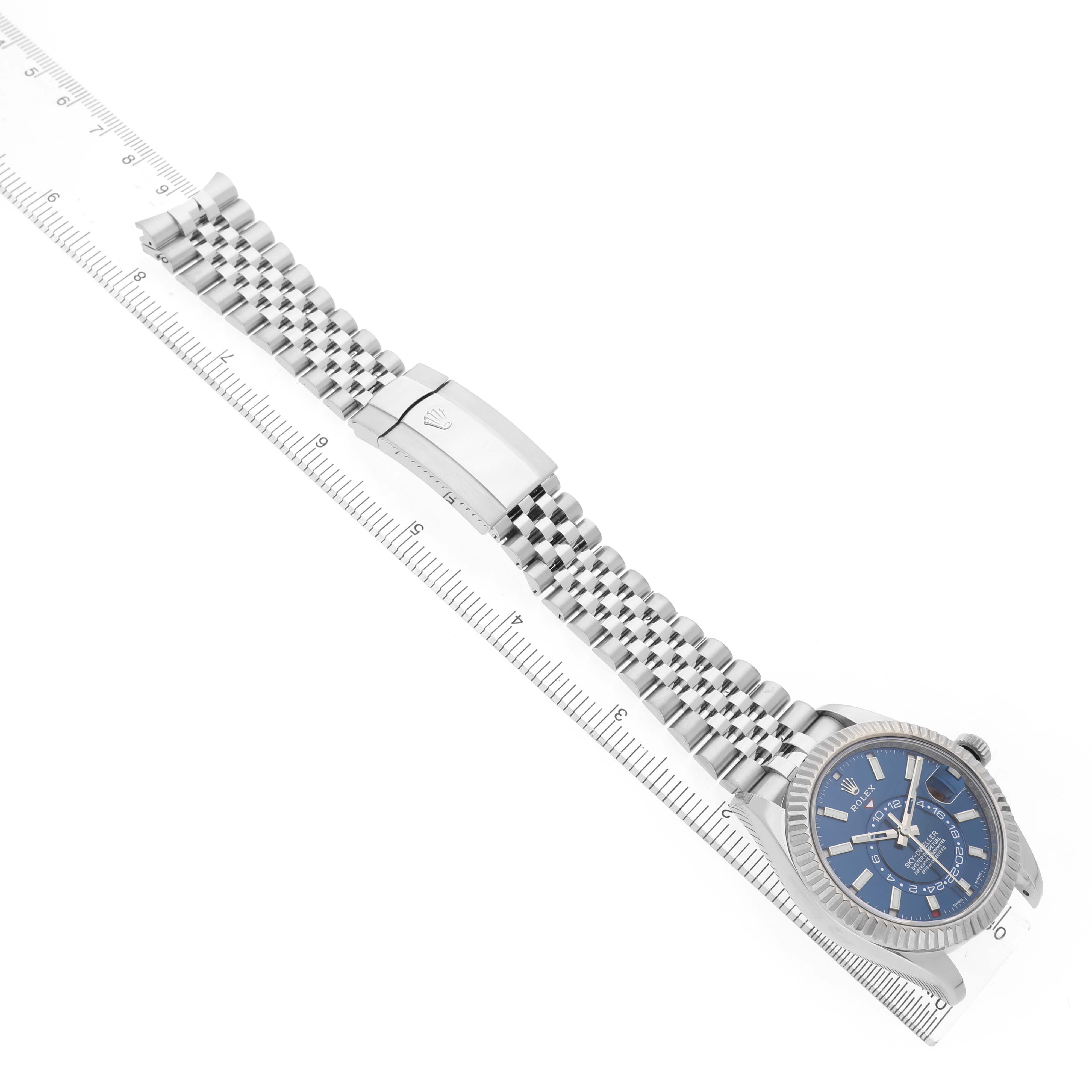 The image shows a Rolex Sky-Dweller 326934 Men's Stainless Steel Blue Dial watch from a top-down angle, highlighting the face, bracelet, and clasp next to a ruler for scale.