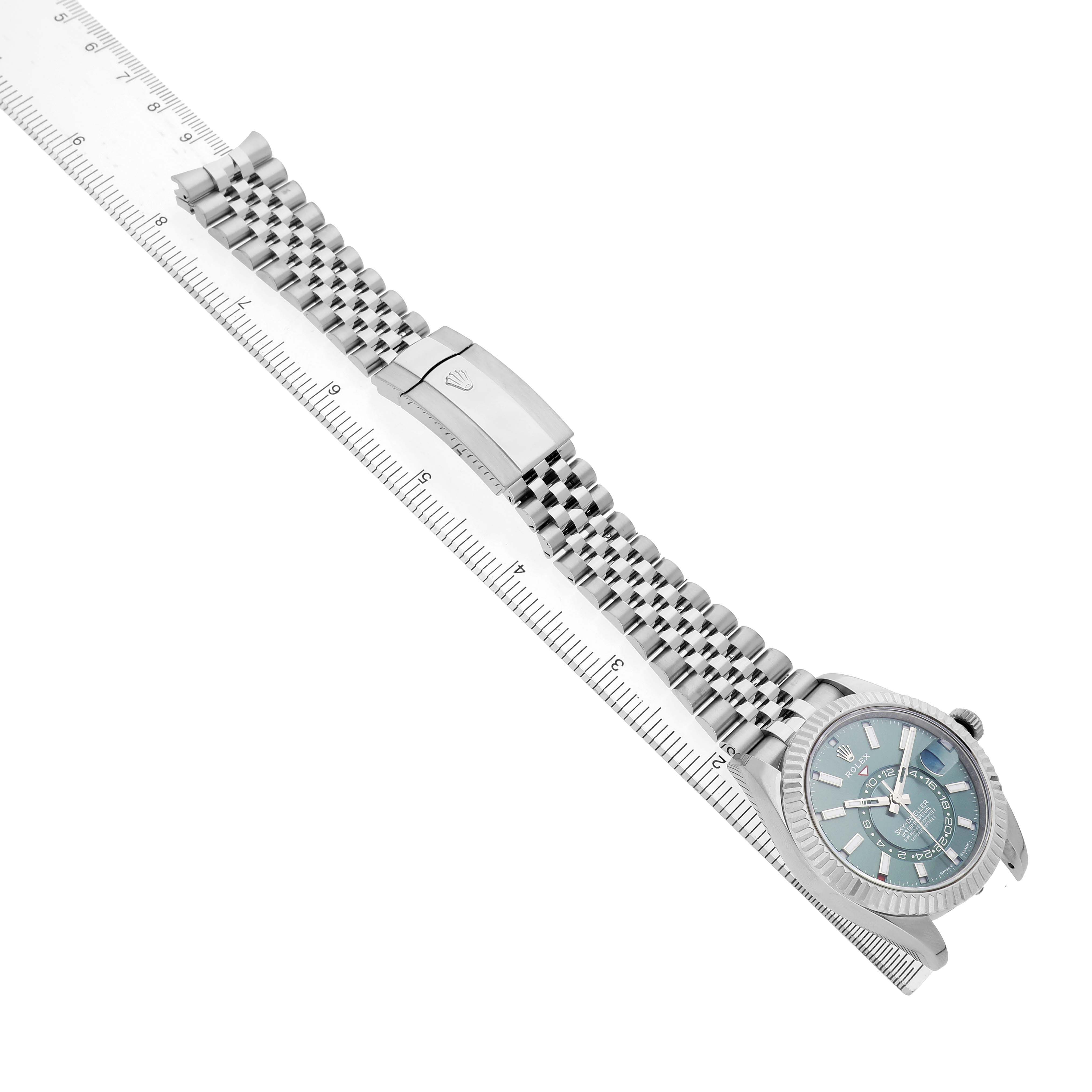 The image shows a Rolex Sky-Dweller 336934 Men's Stainless Steel Green Dial watch at an oblique angle, highlighting the dial, bracelet, and clasp beside a ruler.