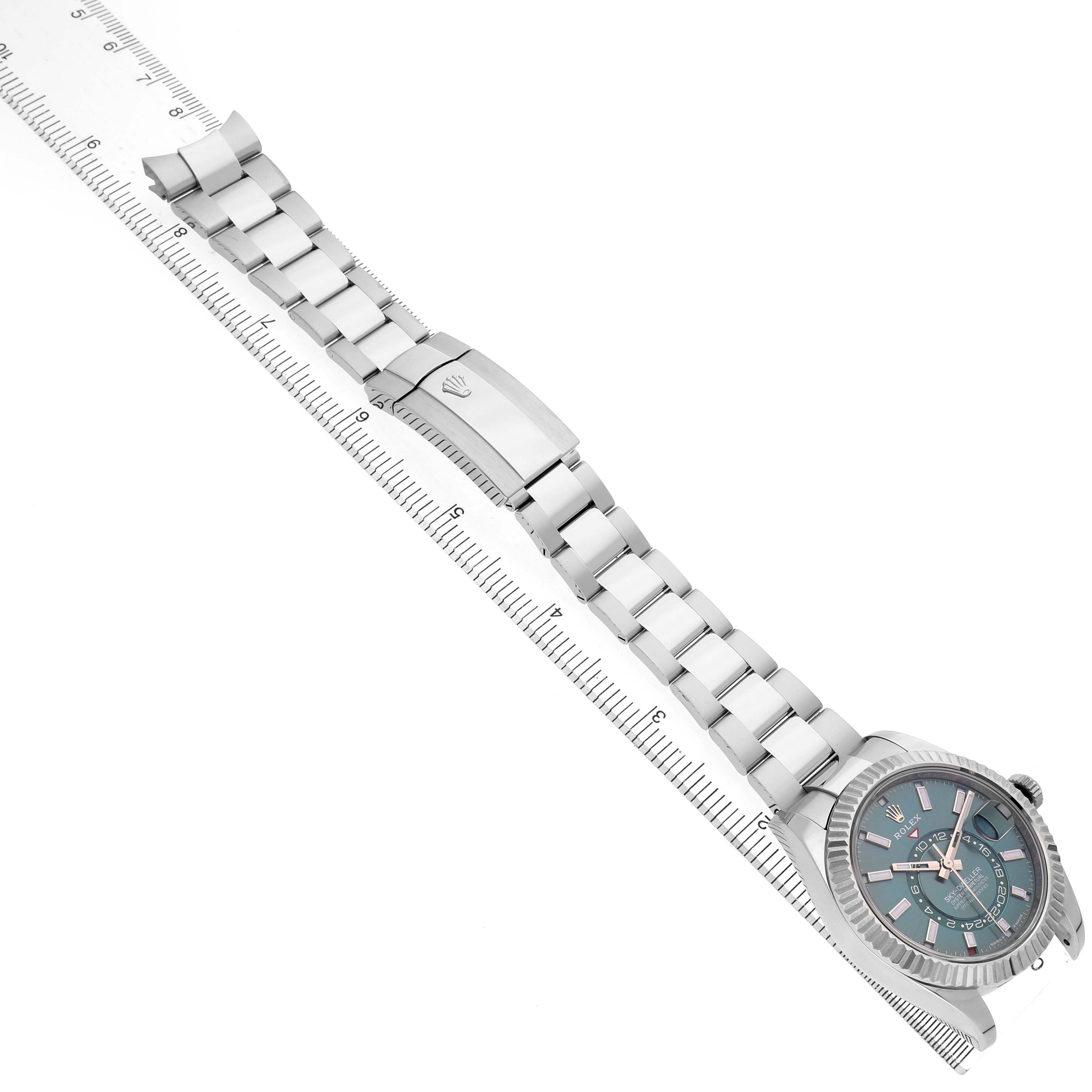 The Rolex Sky-Dweller 336934 Men's Stainless Steel Green Dial watch is shown from a top-down angle, displaying the bracelet, clasp, and face next to a measuring ruler.