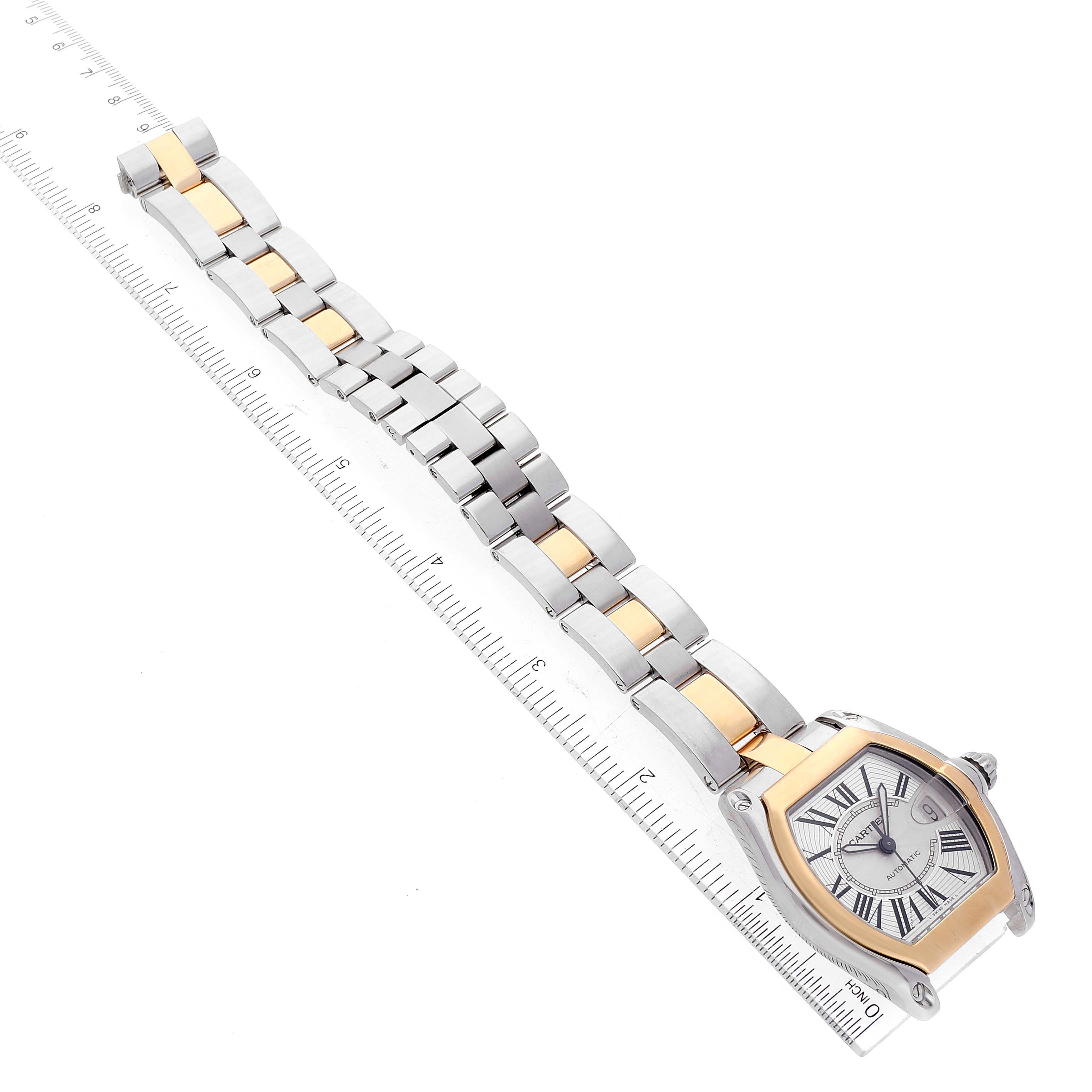 The Cartier Roadster W62031Y4 Men's Steel and Gold (two tone) Silver Dial W62031Y4 Men's Steel and Gold (two tone) Silver Dial watch is shown at an oblique angle, displaying the face, case, and two-tone metal bracelet alongside a ruler.