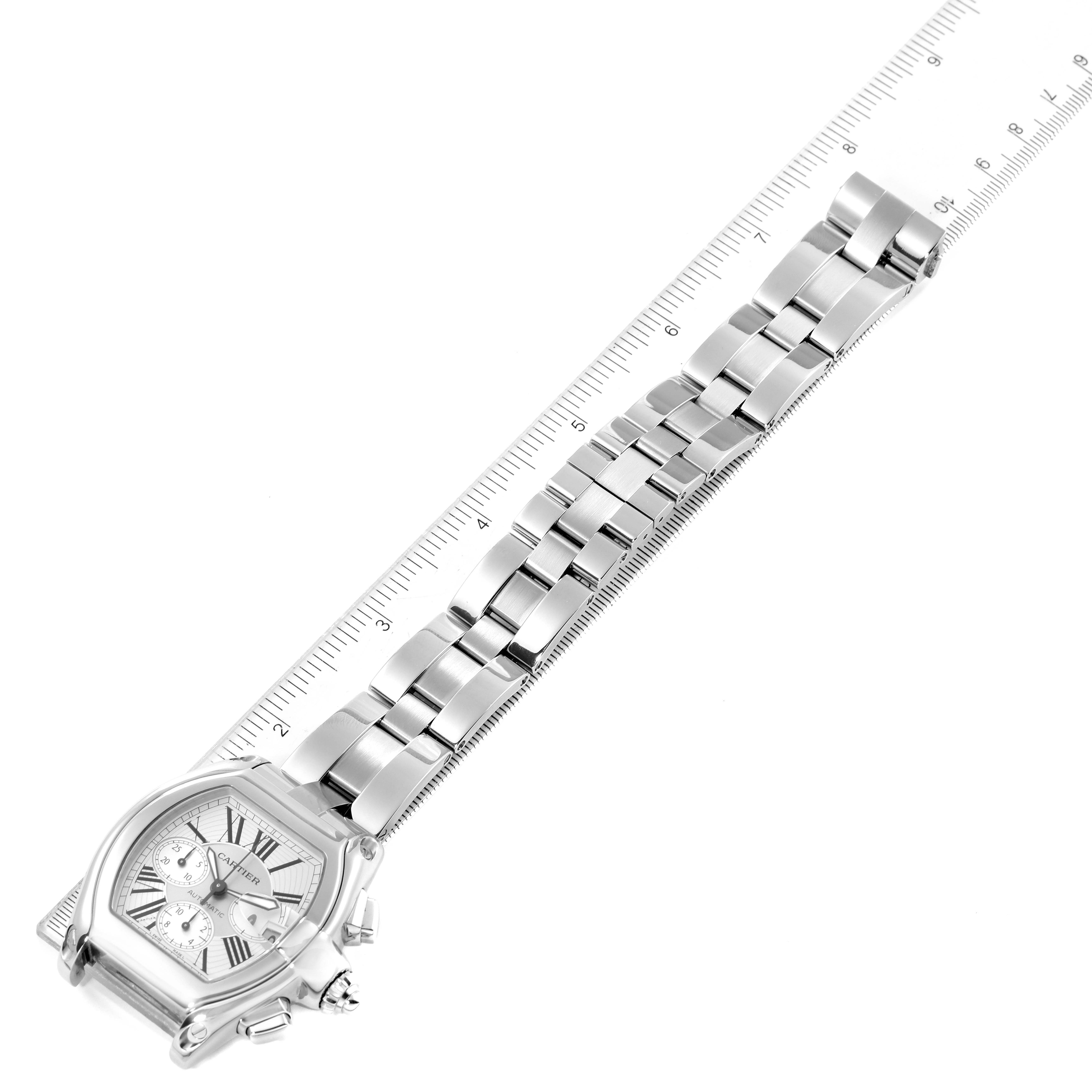 This image shows the Cartier Roadster W62019X6 Men's Stainless Steel Silver Dial W62019X6 Men's Stainless Steel Silver Dial watch laid flat next to a ruler, displaying its dial, case, and bracelet.