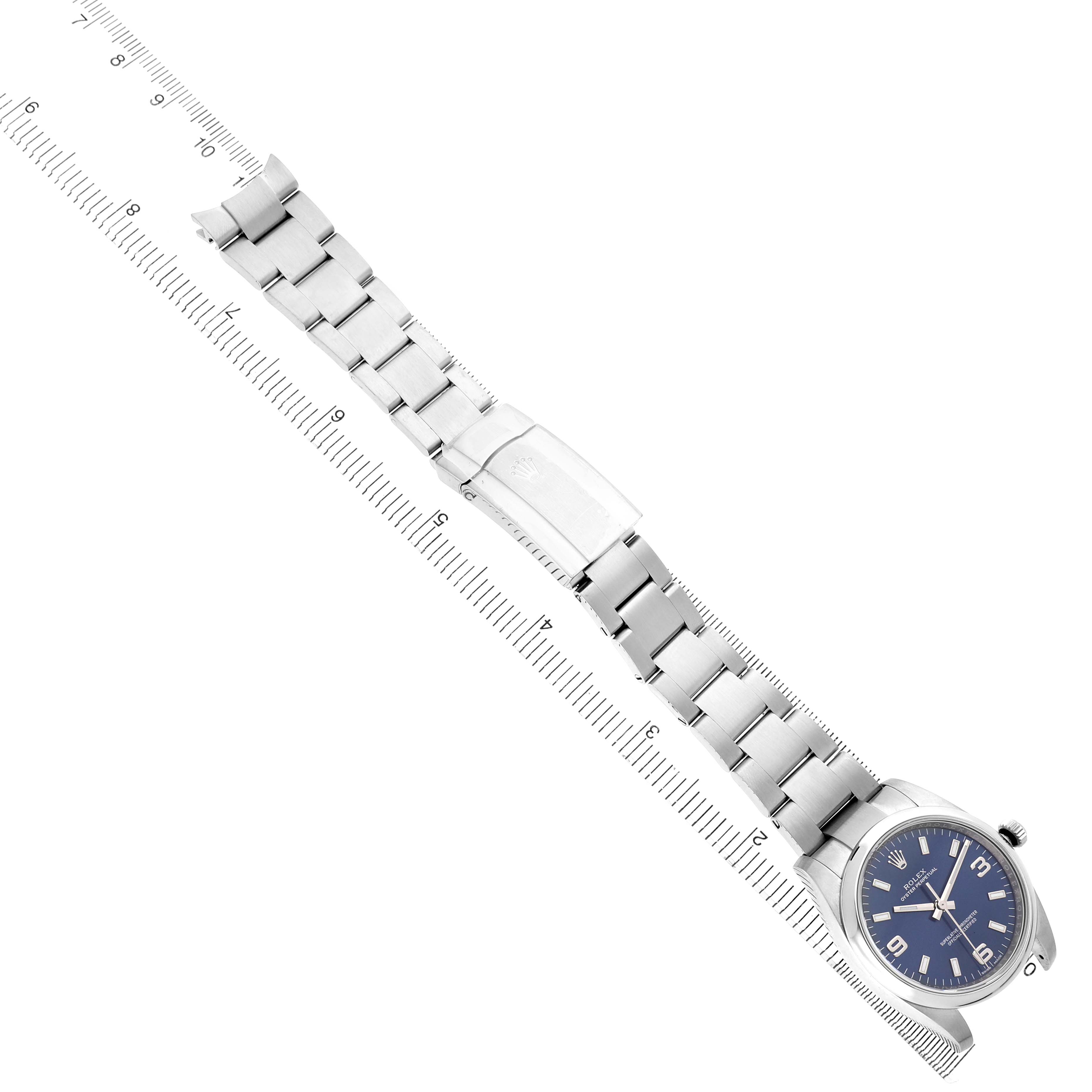 The Rolex Air-King 114200 Men's Stainless Steel Blue Dial watch is shown from a top-down angle, displaying the bracelet, clasp, and dial alongside a ruler for scale.