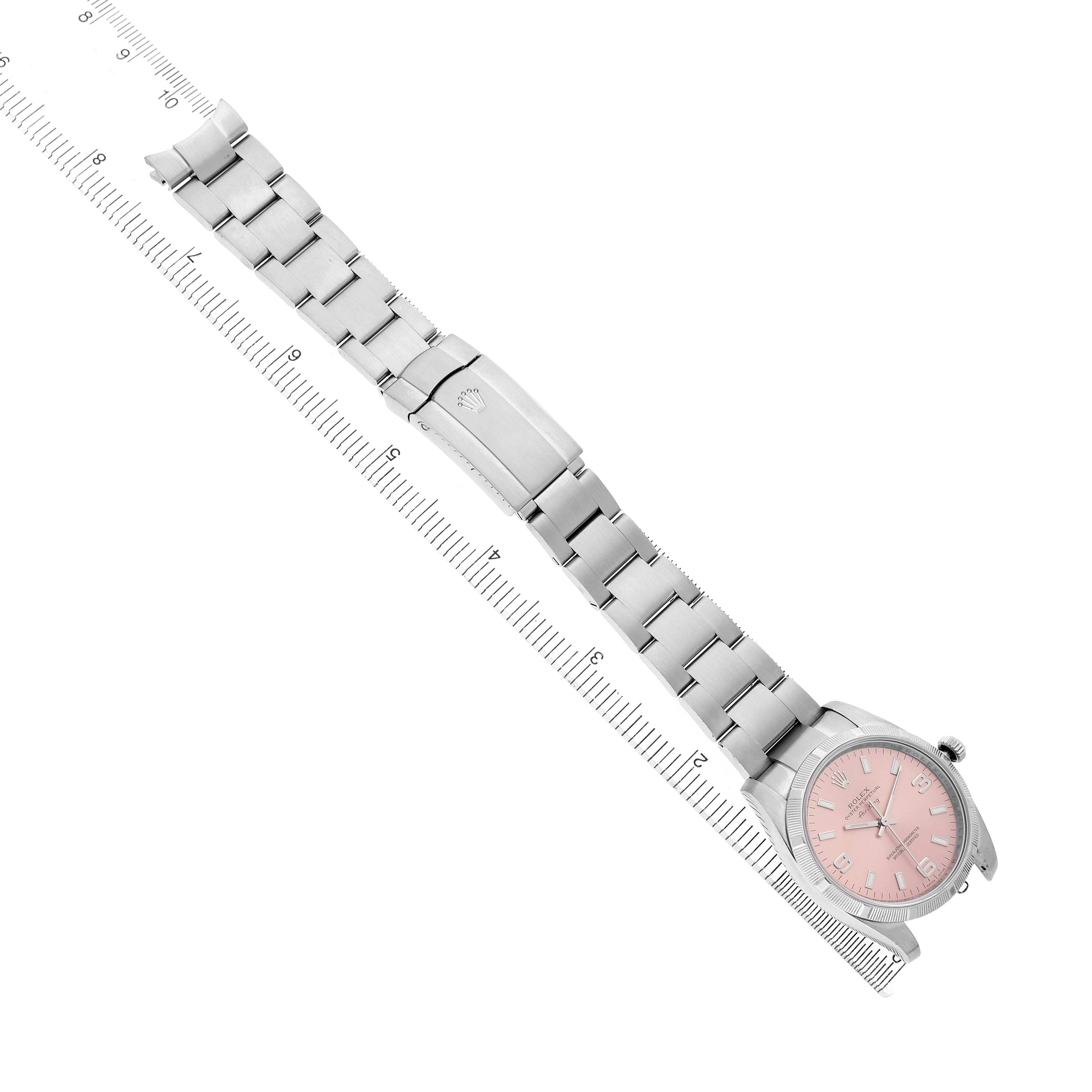 The Rolex Air-King 114210 Men's Stainless Steel Pink Dial watch is shown from an angled top-down view, displaying the bracelet and face alongside a measuring ruler.