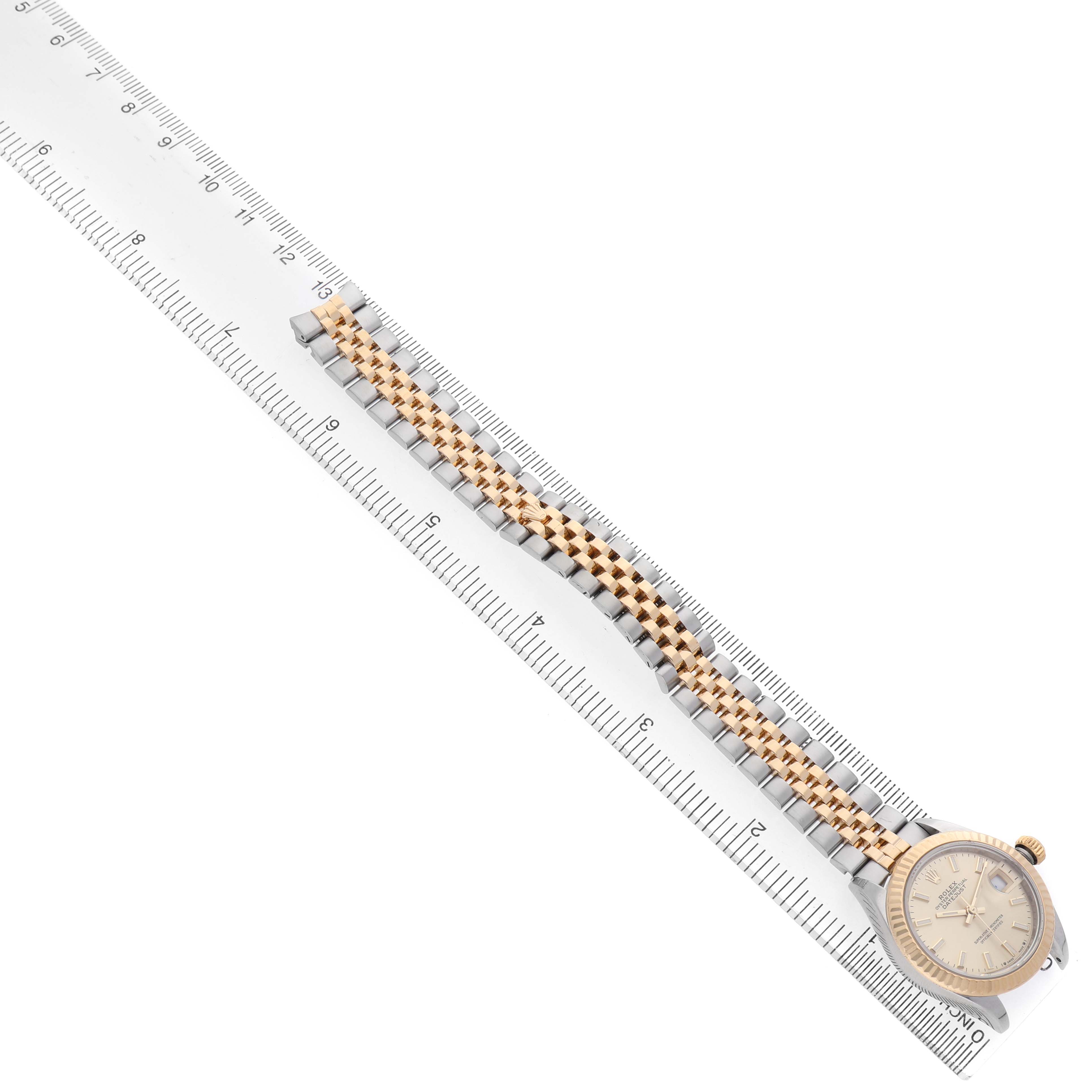 The image shows a Rolex Datejust 279173 Women's Steel and Gold (two tone) Champagne Dial watch at a diagonal angle, highlighting the face and two-tone bracelet alongside a ruler.