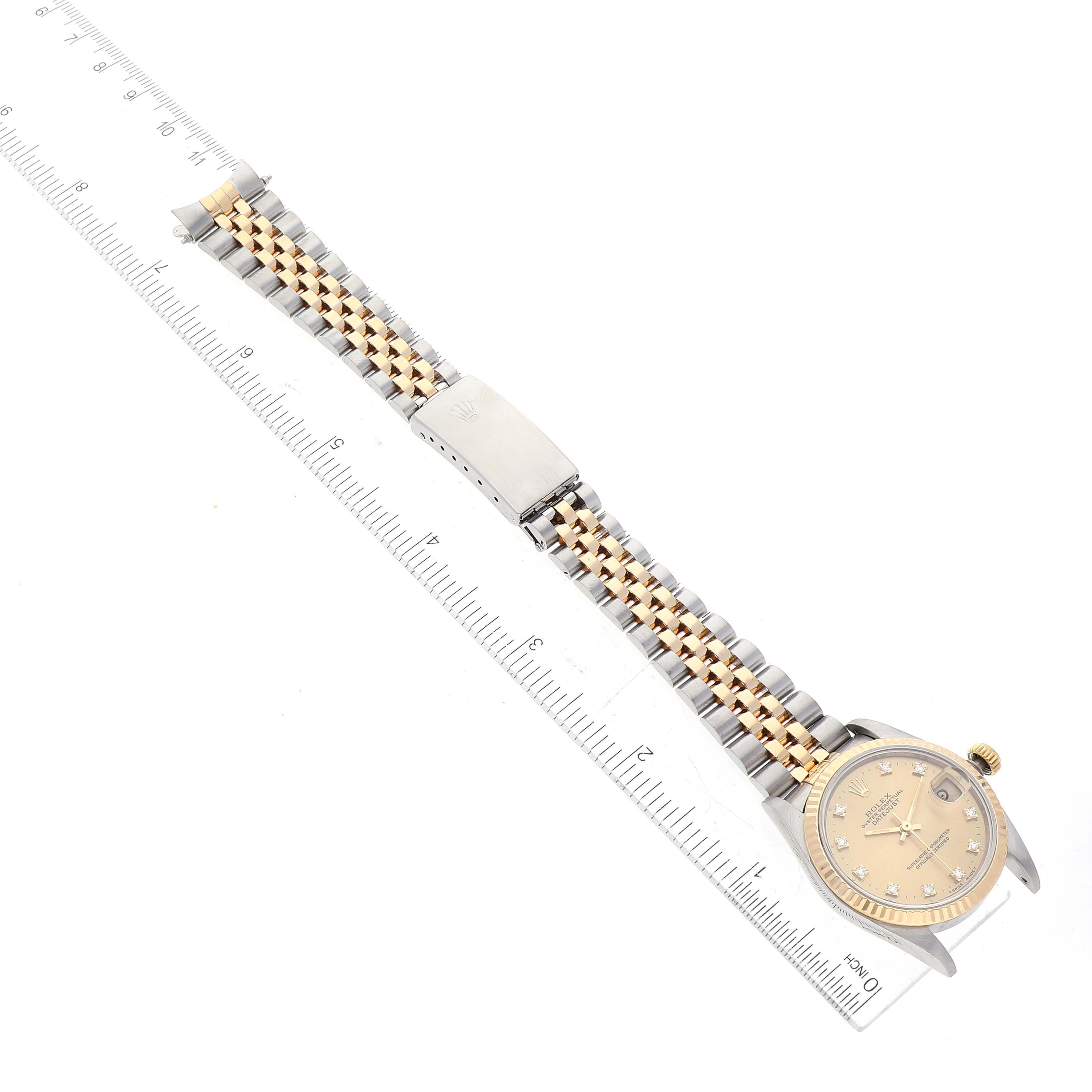 The Rolex Mid-Size 68273 Women's Steel and Gold (two tone) Champagne Dial 68273 Women's Steel and Gold (two tone) Champagne Dial model watch is shown from an overhead angle with a metal bracelet and a ruler beside it.