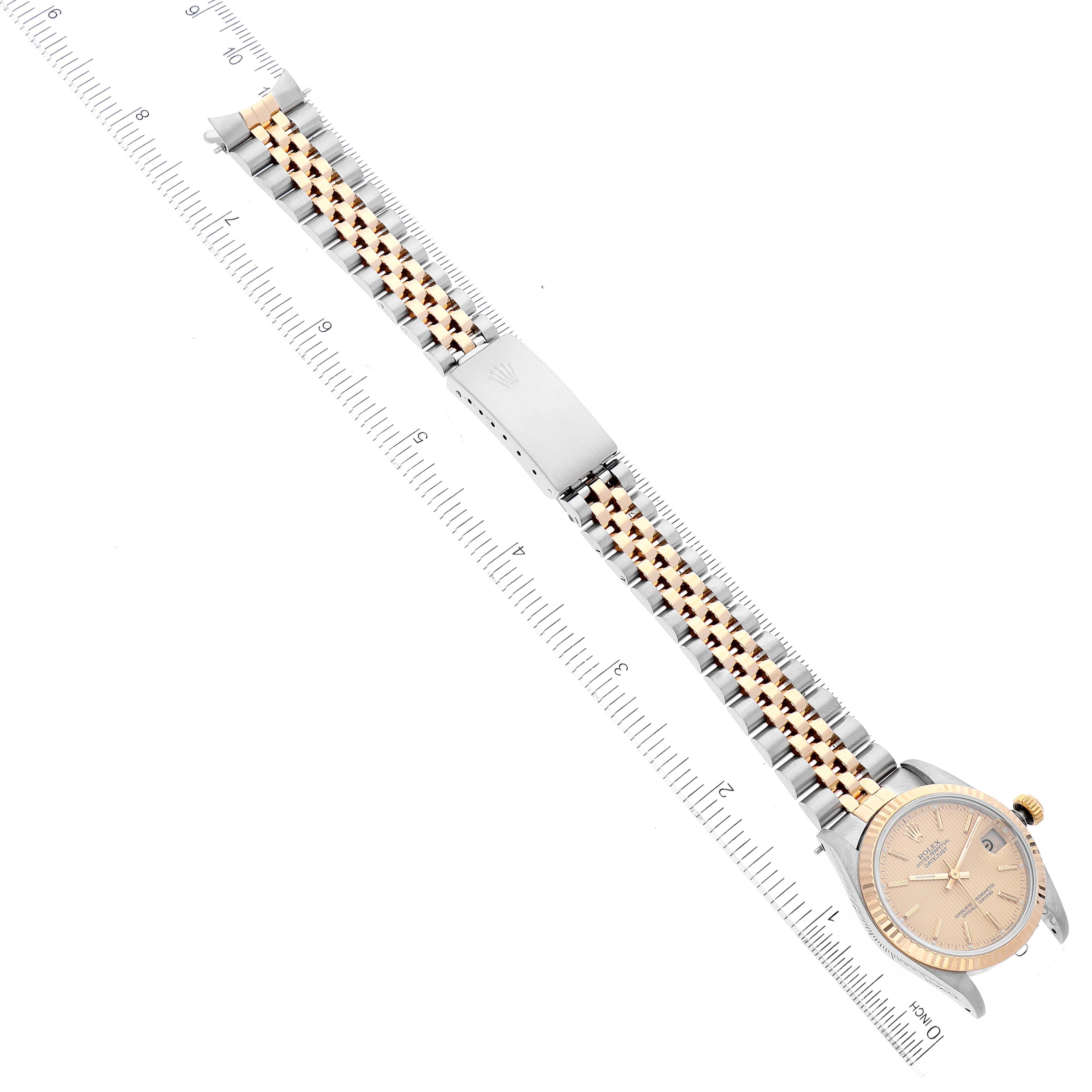 The image shows a full view of the Rolex Mid-Size 68273 Women
s Steel and Gold (two tone) Champagne Dial 68273 Women
s Steel and Gold (two tone) Champagne Dial watch, displaying its face, bracelet, clasp, and a ruler for scale.