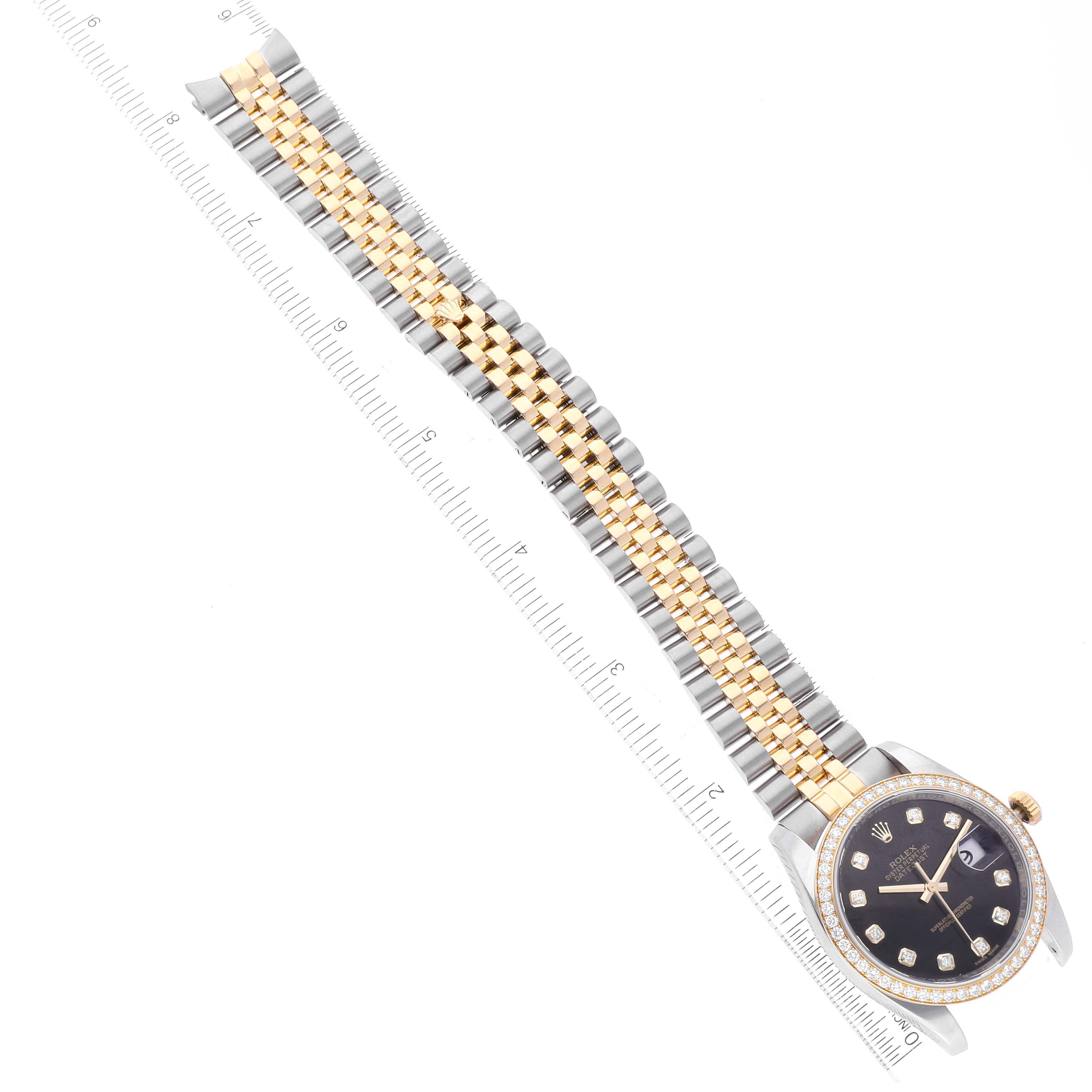 The Rolex Datejust 116243 Men's Steel and Gold (two tone) Black Dial 116243 Men's Steel and Gold (two tone) Black Dial watch is photographed from a top view, displaying the dial, bezel, and two-tone bracelet alongside a measuring scale.