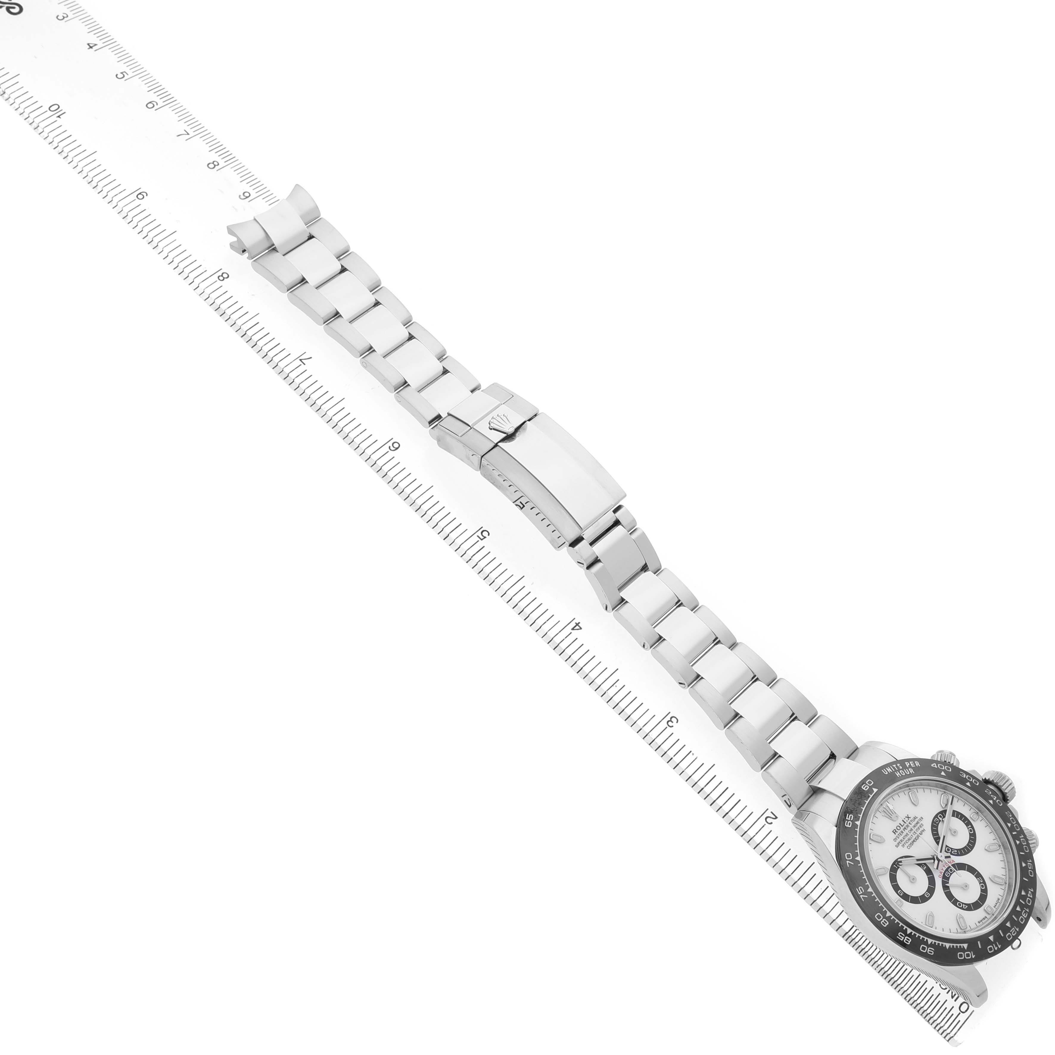 The Rolex Daytona 116500 Men's Stainless Steel White Dial watch is shown at a slight diagonal, displaying the dial, bezel, bracelet, and clasp alongside a ruler.
