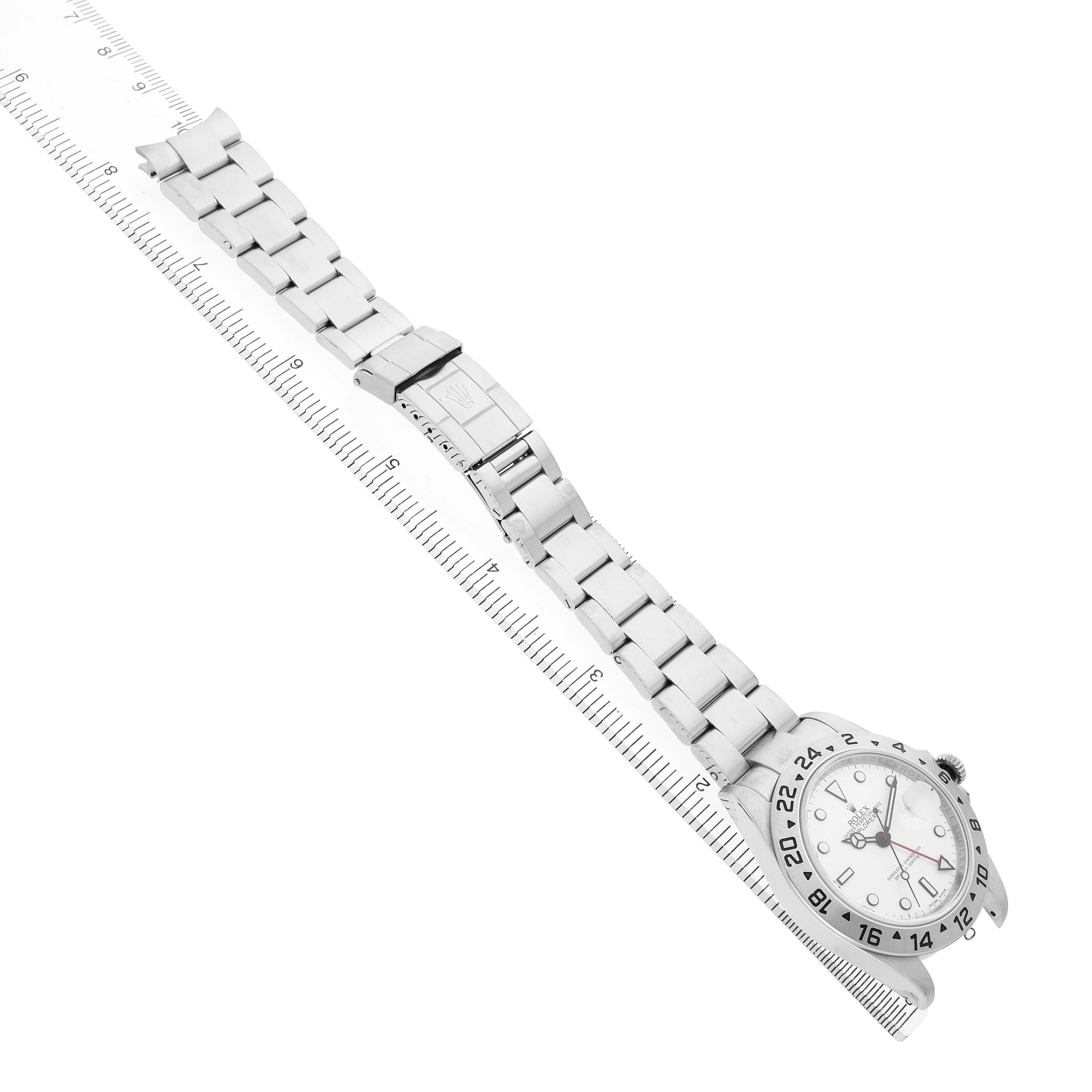 The Rolex Explorer 16570 Men's Stainless Steel White Dial watch is shown from a top-down angle, displaying the face, bracelet, and clasp beside a ruler for scale.
