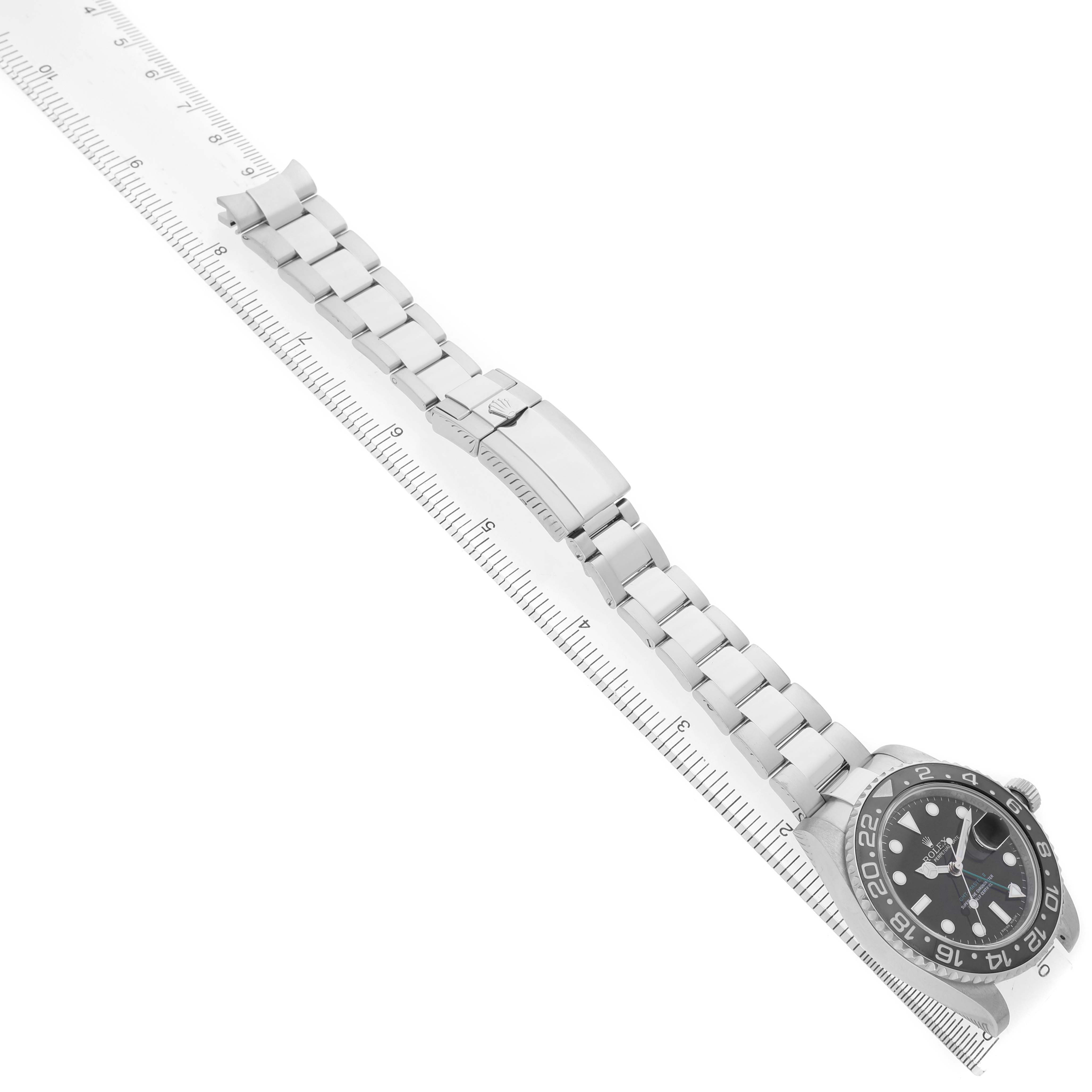 The image shows a top-down view of a Rolex GMT-Master 116710 Men's Stainless Steel Black Dial watch laid flat on a ruler, highlighting the dial and bracelet.