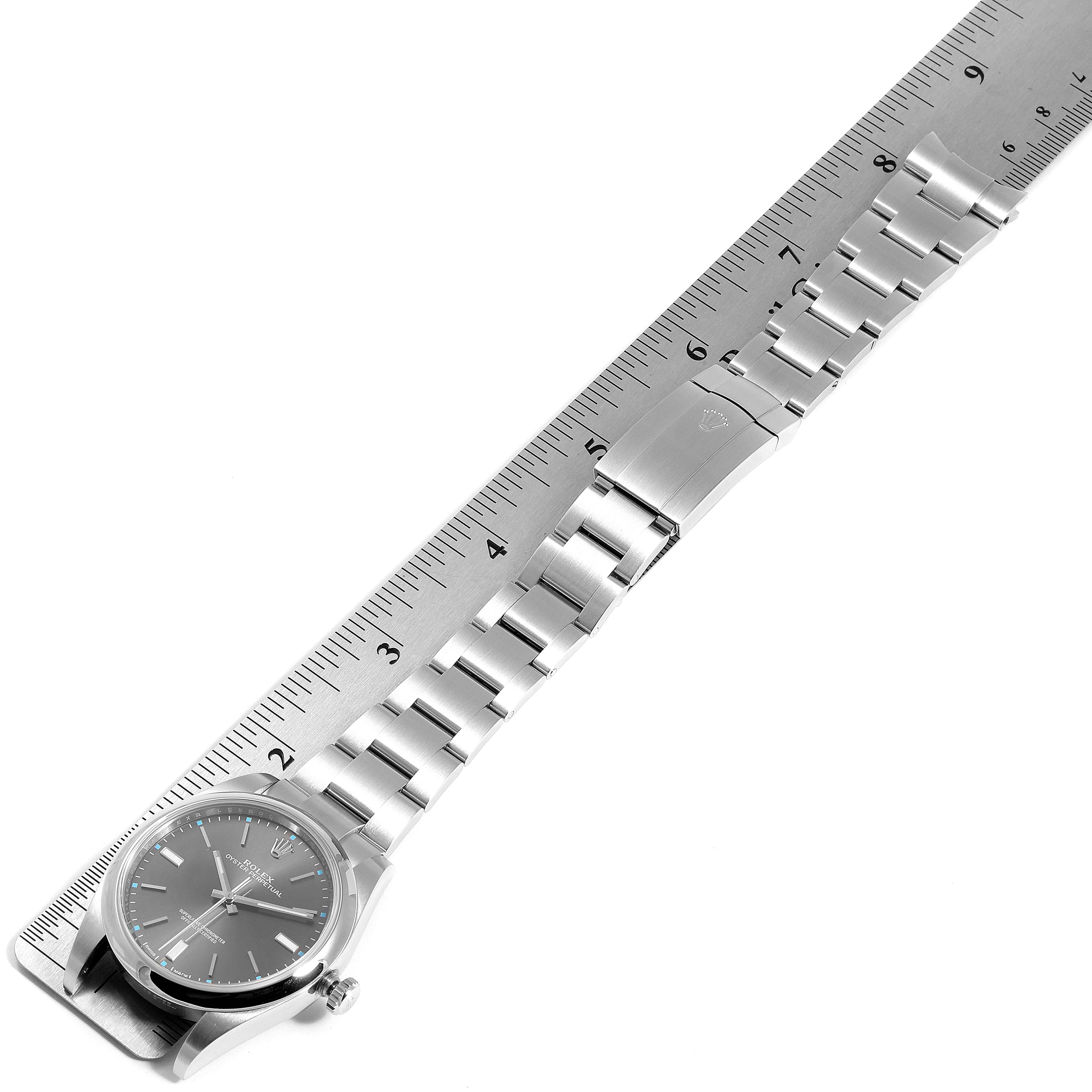 The image shows a Rolex Oyster Perpetual 114300 Men's Stainless Steel Silver Dial 114300 Men's Stainless Steel Silver Dial watch laid flat beside a ruler, displaying the watch face and stainless steel bracelet.