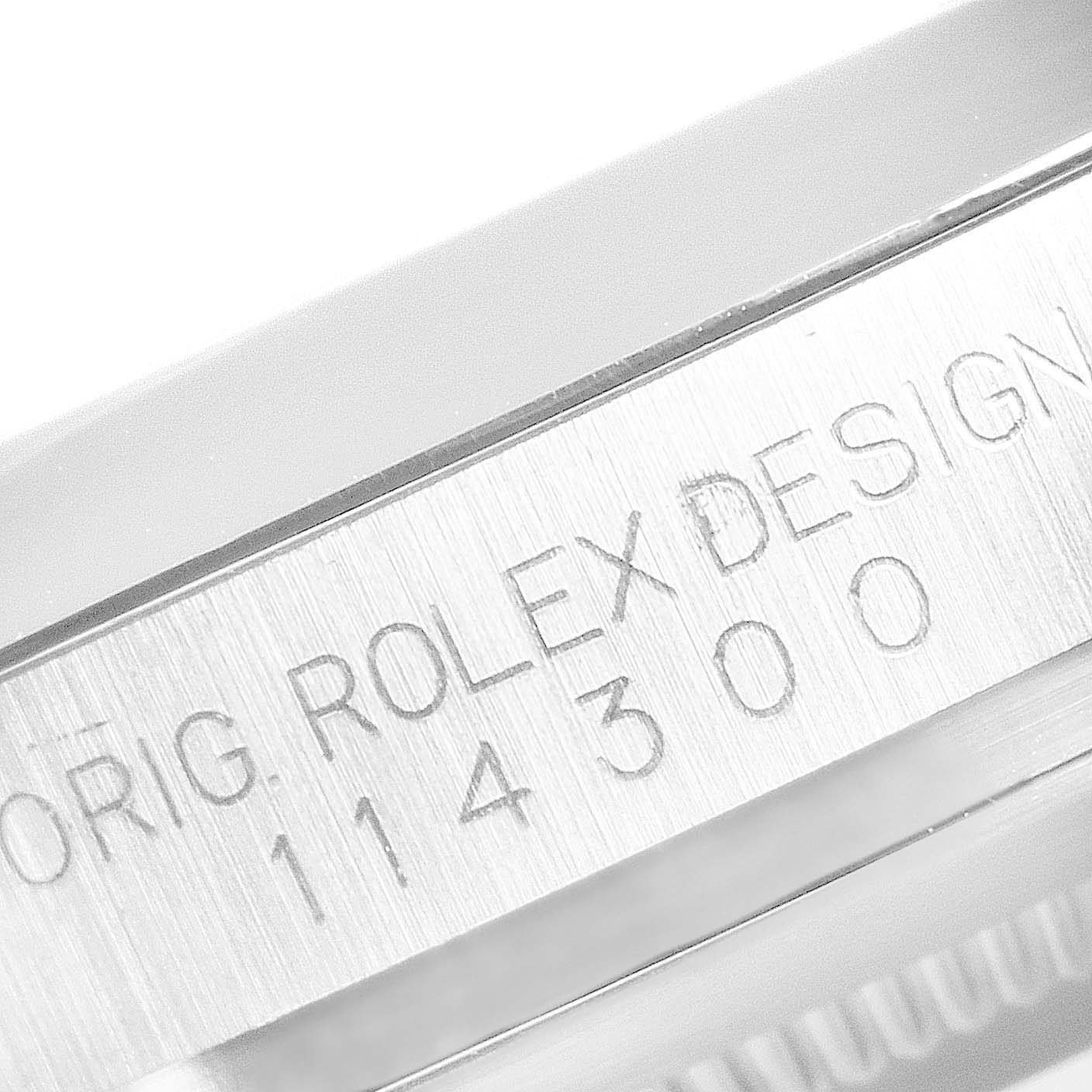 The image shows the side of a Rolex Oyster Perpetual 114300 Men's Stainless Steel Grey Dial, focusing on the engraved serial and model numbers.