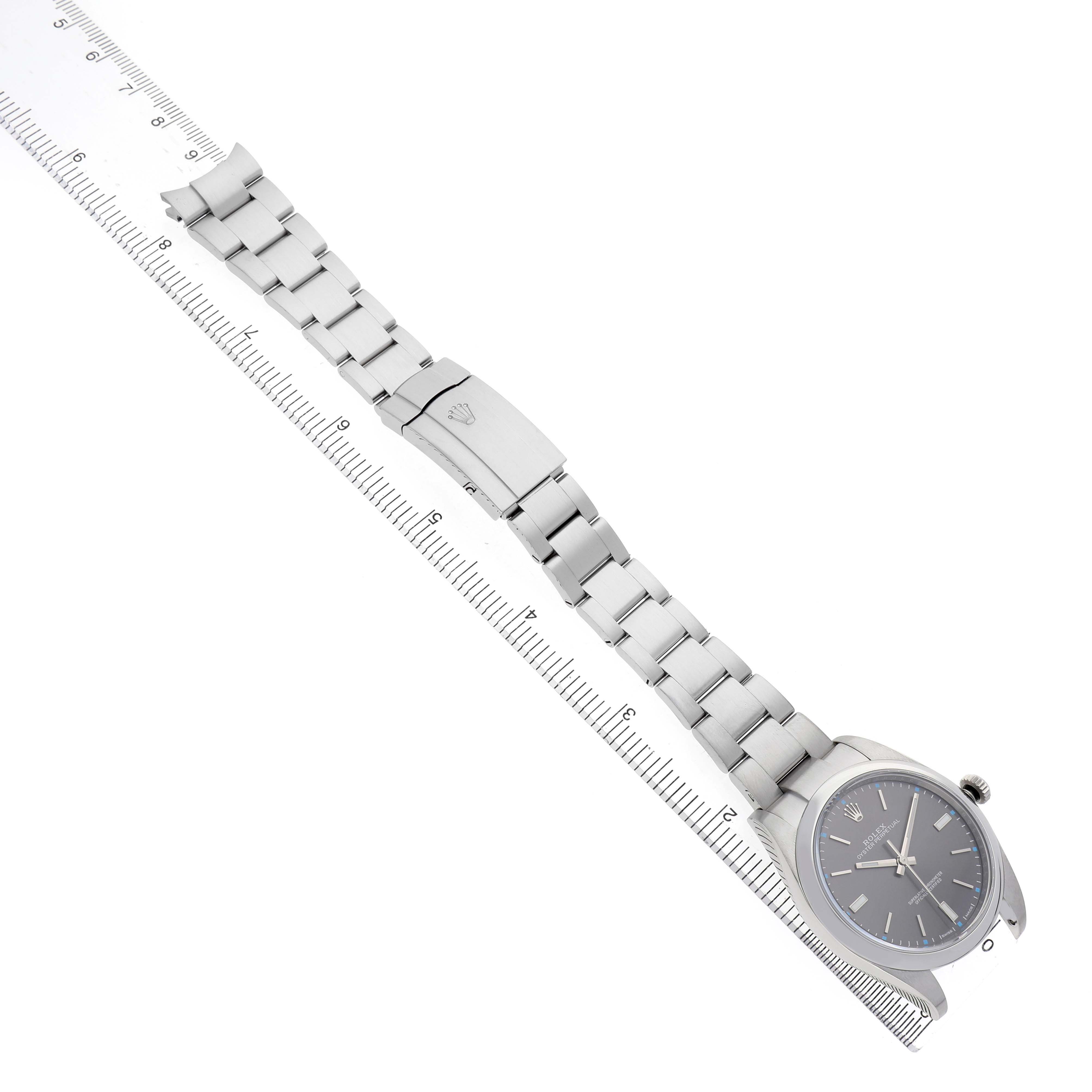 The Rolex Oyster Perpetual 114300 Men's Stainless Steel Grey Dial watch is shown from a top view, displaying the dial, bezel, bracelet, and clasp alongside a ruler.