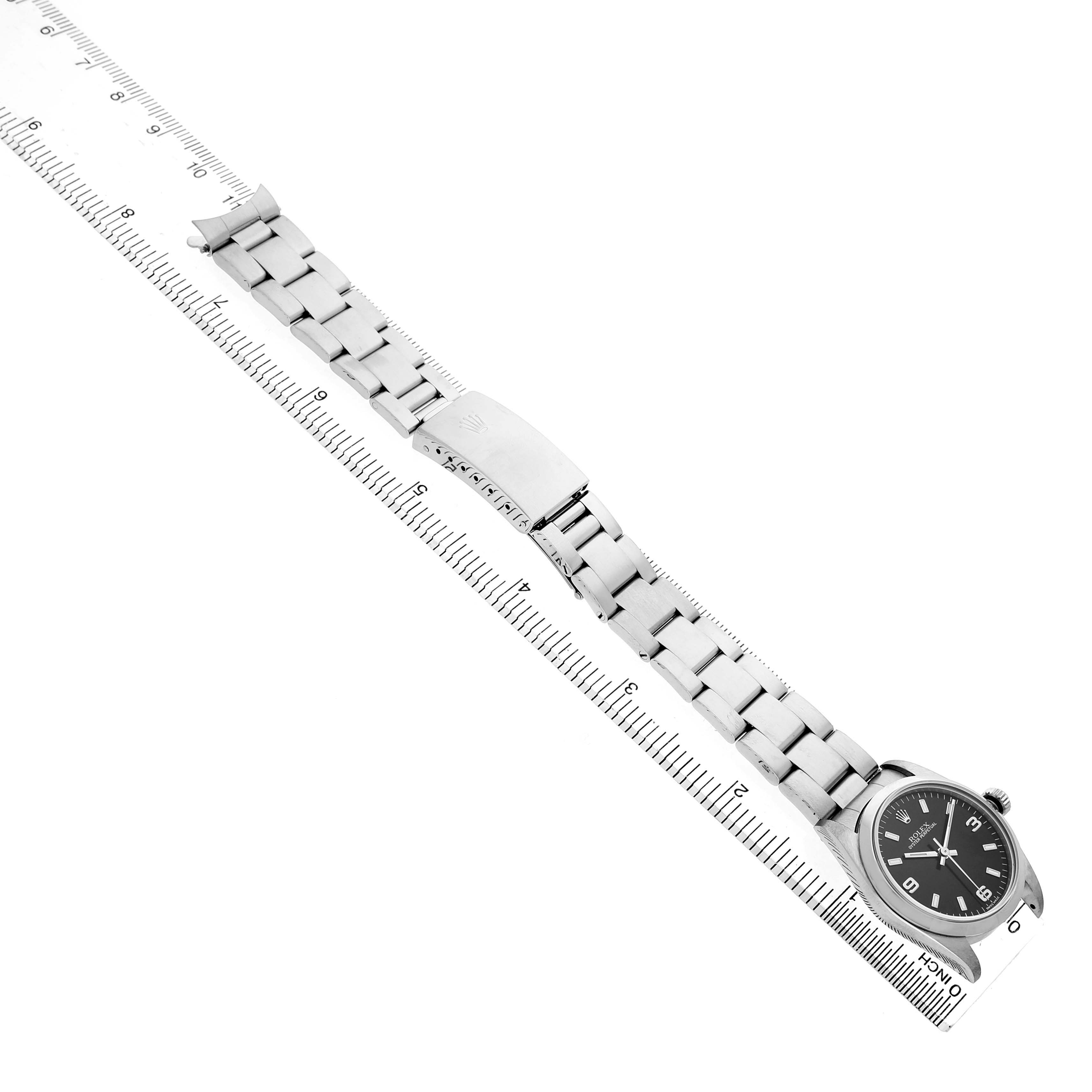 The Rolex Mid-Size 77080 Women's Stainless Steel Black Dial model watch is shown from an angled top view, displaying its bracelet, case, and clasp alongside a ruler.