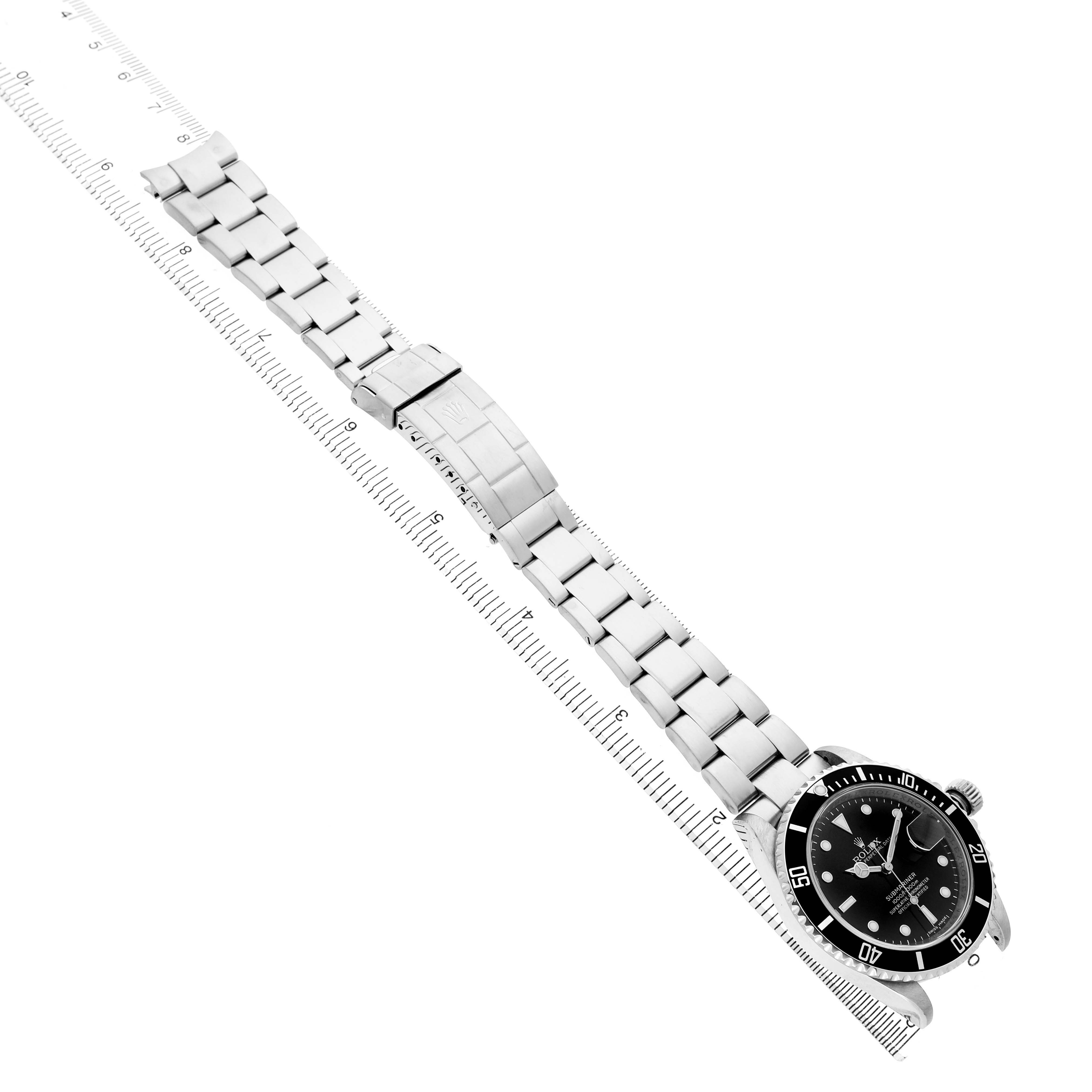 The Rolex Submariner 16610 Men's Stainless Steel Black Dial is shown from a diagonal top view, displaying the full watch, bracelet, and clasp alongside a ruler.