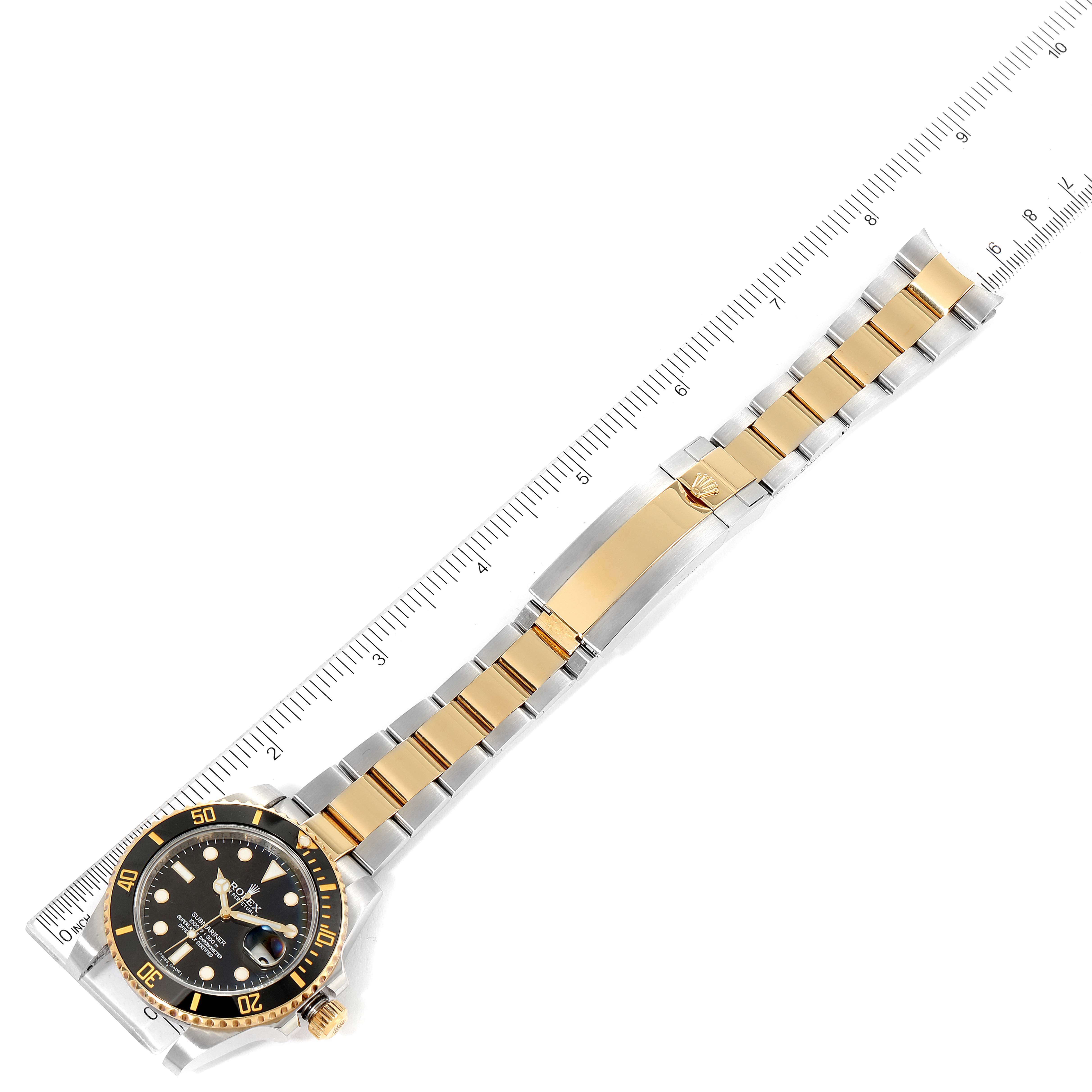 The image shows a top-down view of a Rolex Submariner 116613 Men
s Steel and Gold (two tone) Black Dial 116613 Men
s Steel and Gold (two tone) Black Dial watch, including its dial, bezel, and two-tone bracelet with a ruler alongside.