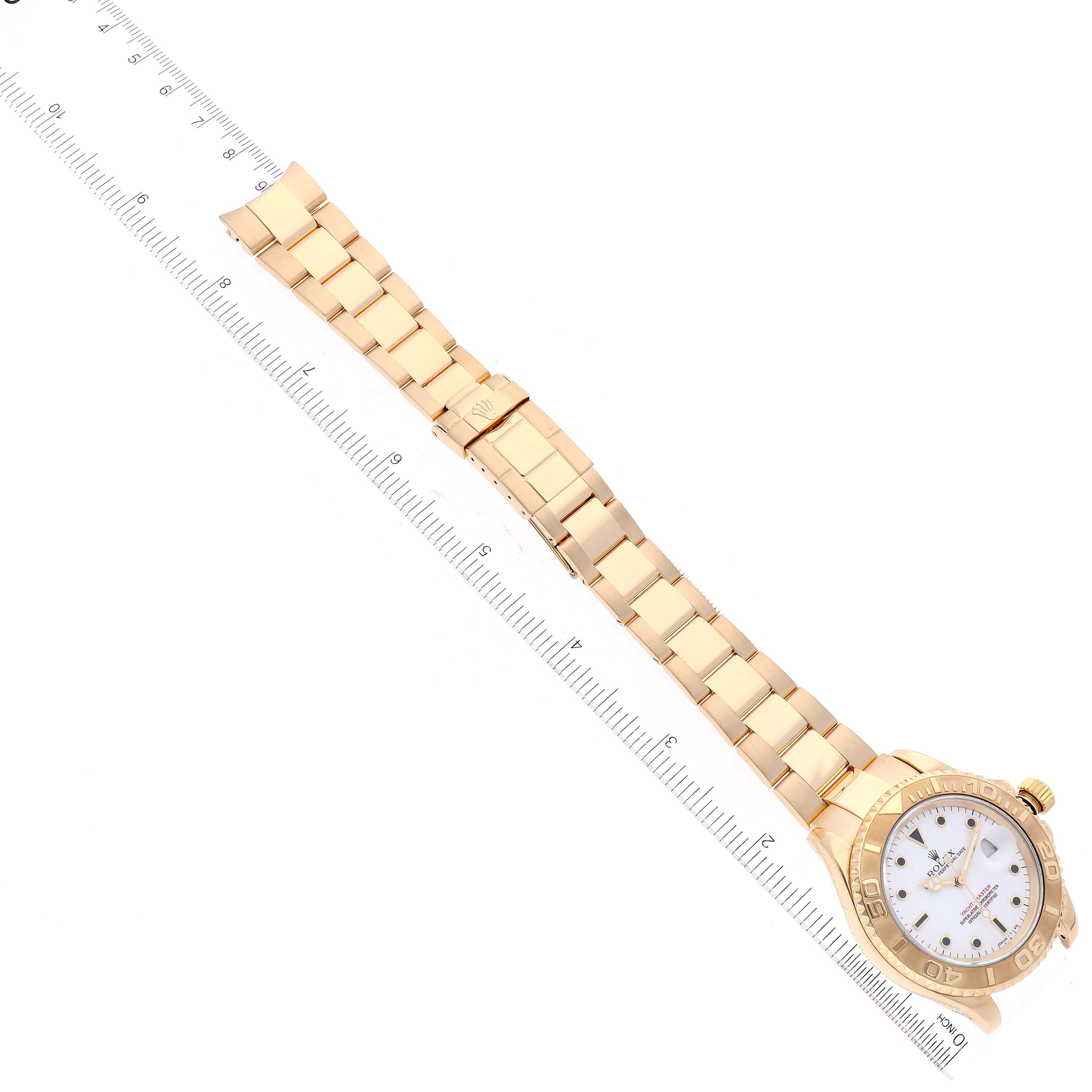 The image shows a Rolex Yacht-Master 16628 Men's Yellow Gold White Dial watch laid flat with a focus on the face, bracelet, and a ruler for scale.