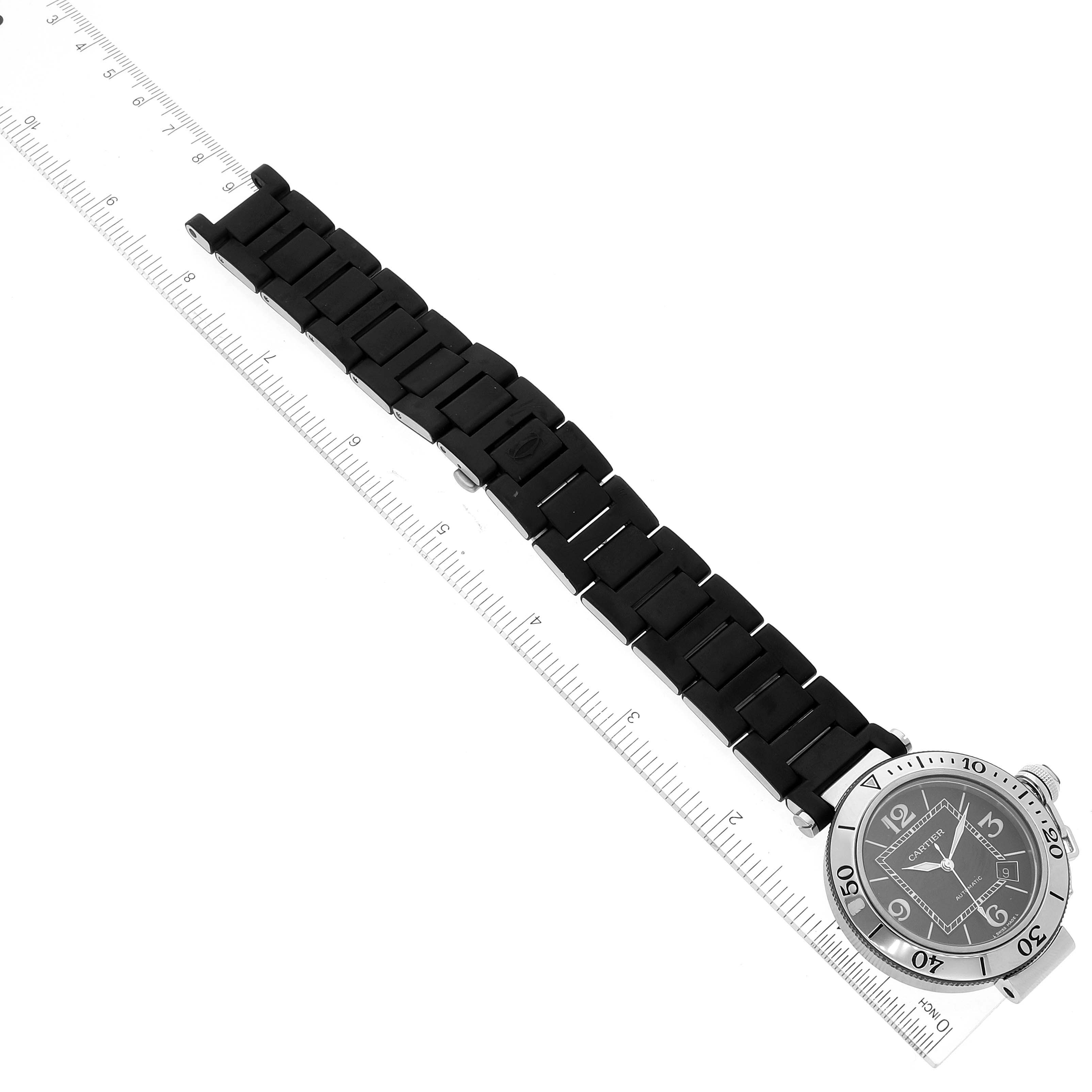 The image shows a top-down angle of a Cartier Pasha W31077U2 Men's Stainless Steel Black Dial W31077U2 Men's Stainless Steel Black Dial watch, highlighting its face, bezel, and bracelet alongside a ruler for scale.