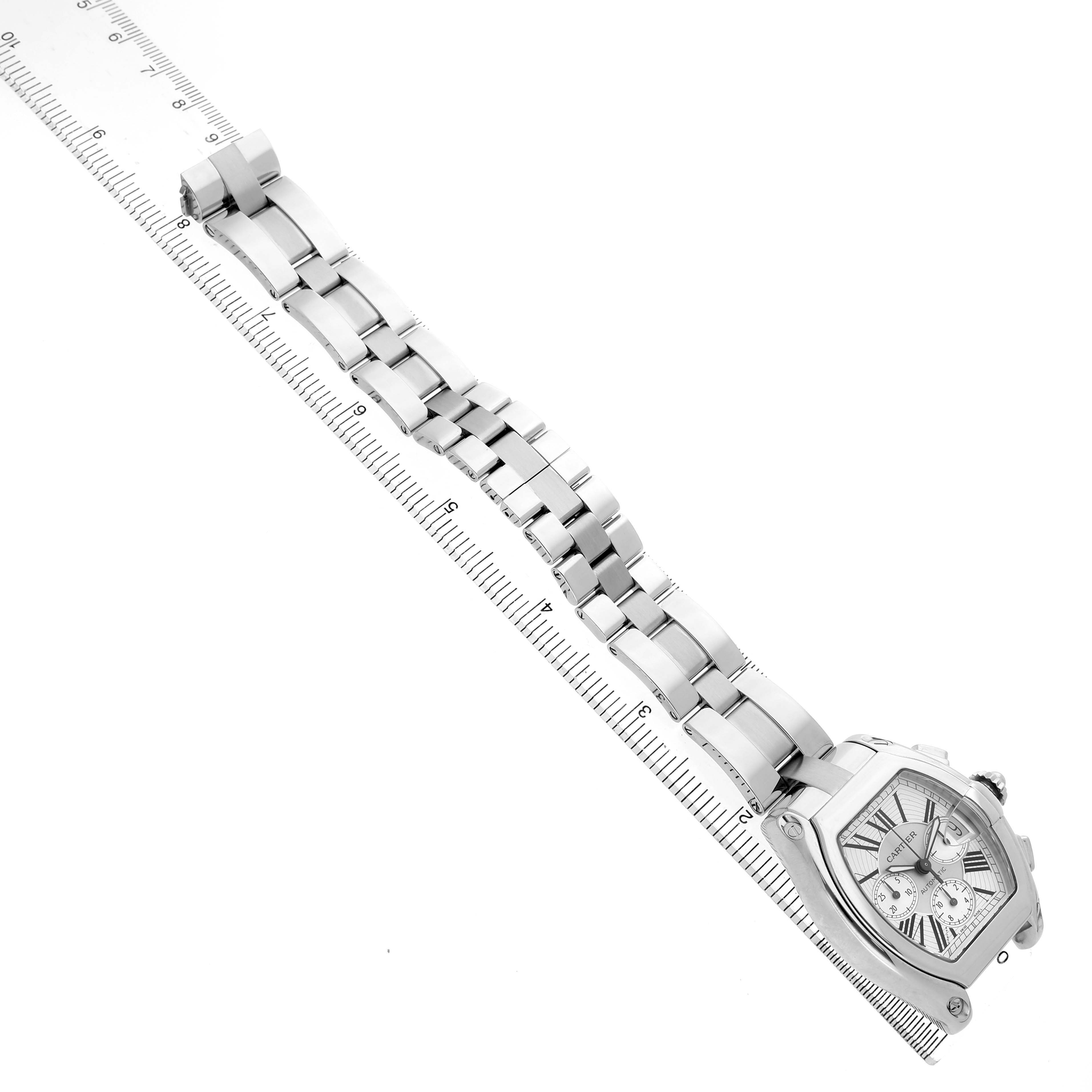 The Cartier Roadster W62019X6 Men's Stainless Steel Silver Dial watch is shown from a top view, displaying the face, bracelet, and ruler for scale.