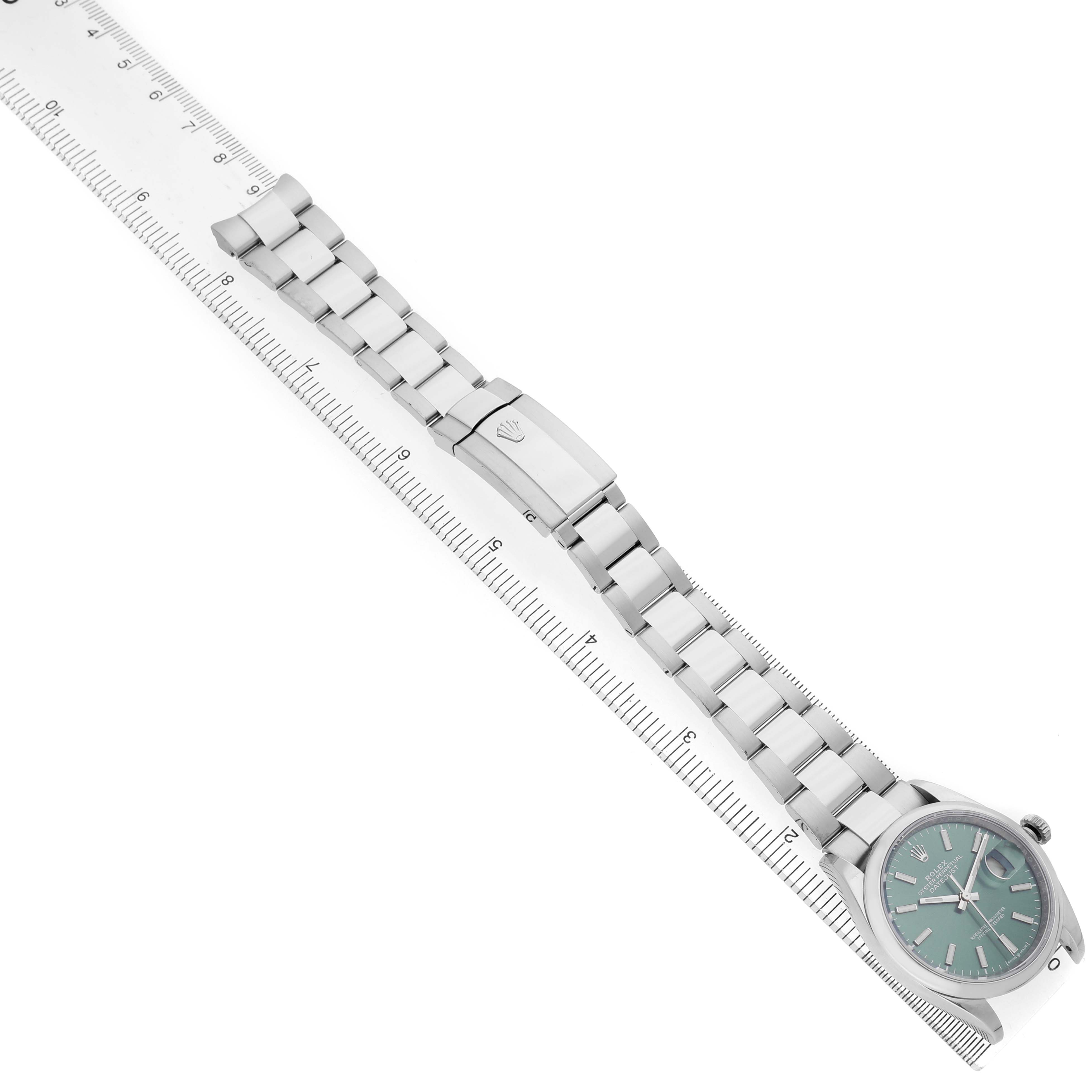 The Rolex Datejust 126200 Men's Stainless Steel Green Dial watch is shown from a top-down angle, displaying its full bracelet and face beside a ruler for scale.