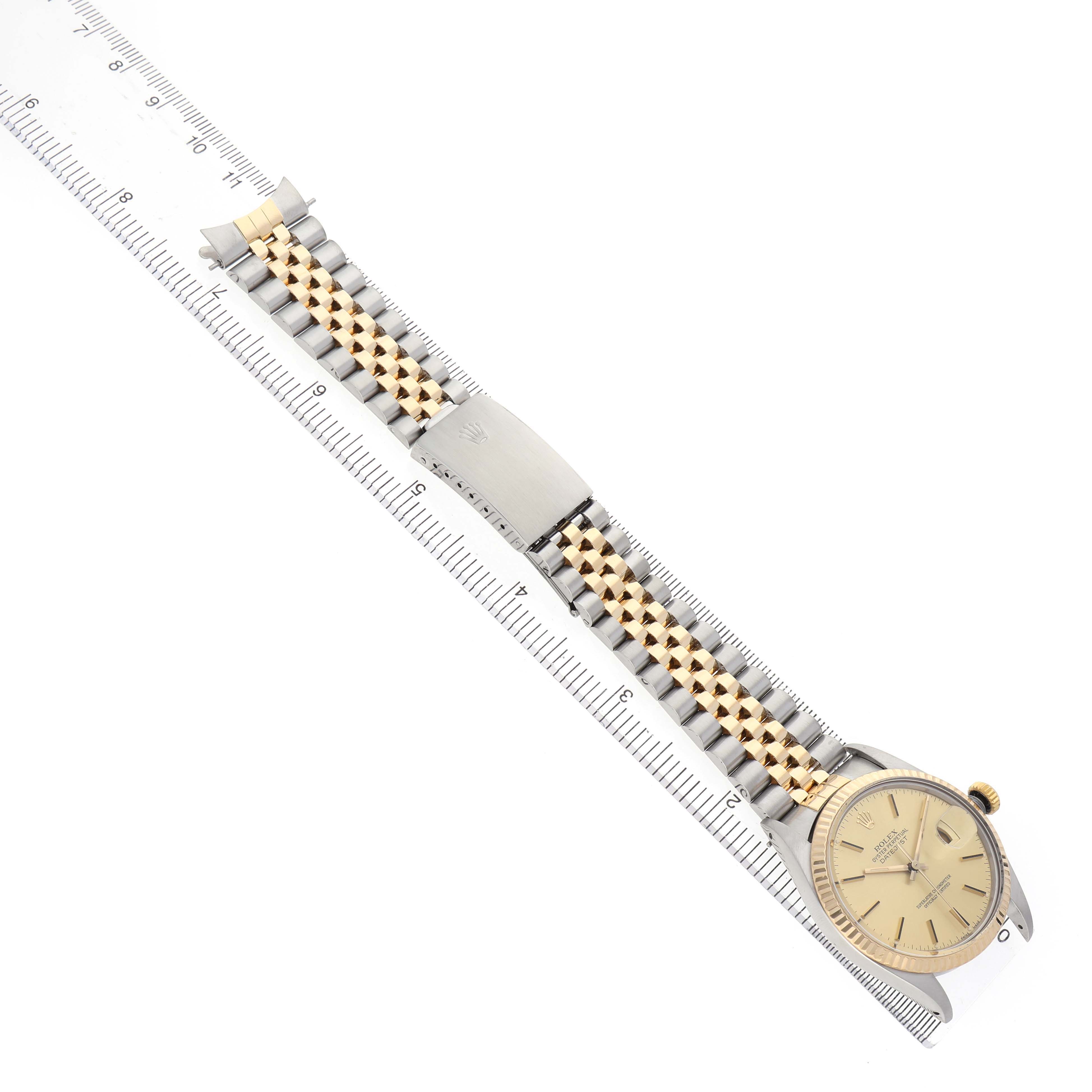 The Rolex Datejust 16013 Men's Steel and Gold (two tone) Champagne Dial watch is shown laid flat with a focus on the bracelet and clasp, aligned with a ruler for scale.