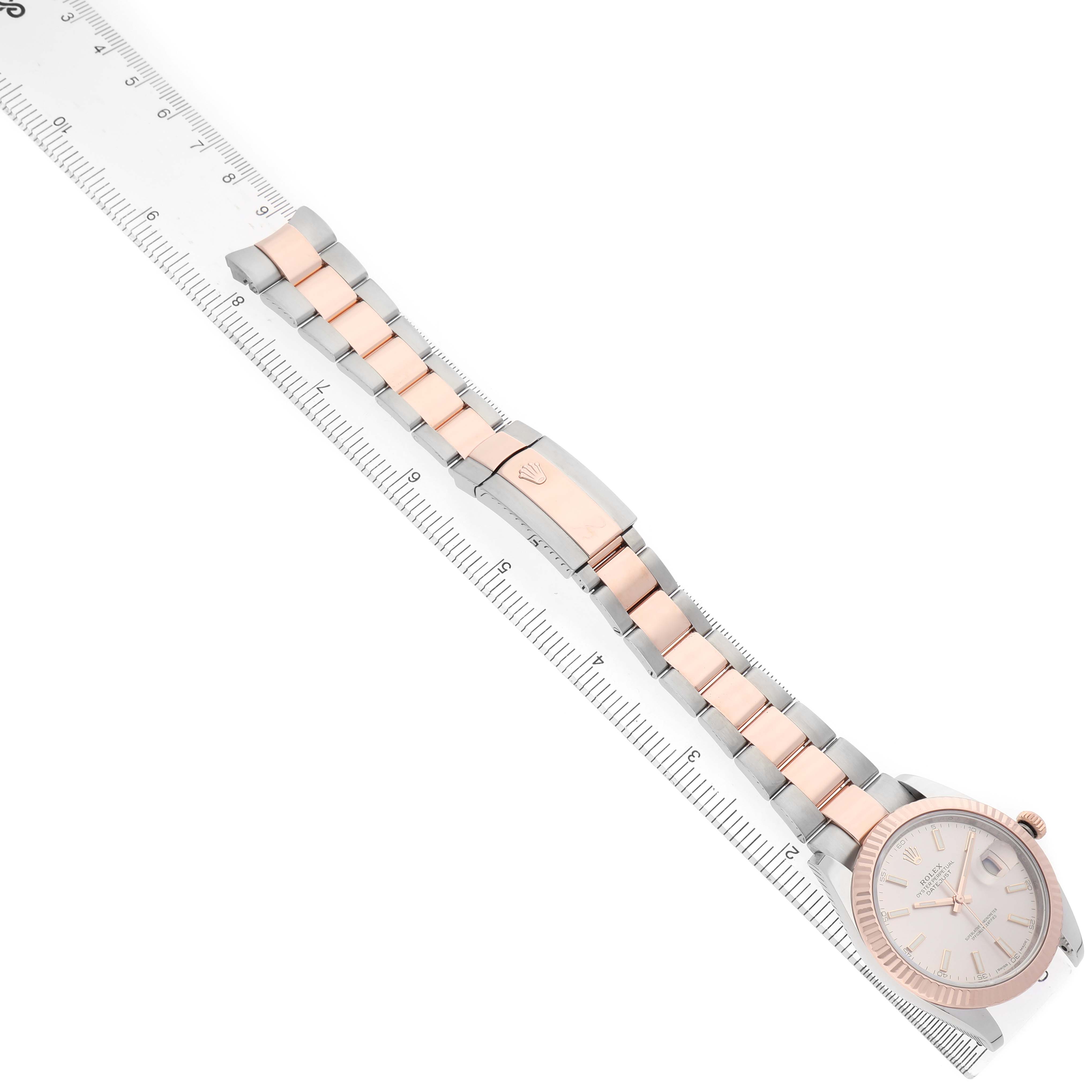 The Rolex Datejust 126331 Men's Steel and Gold (two tone) Pink Dial watch is shown from an angled side view, highlighting the face, bracelet, clasp, and a ruler for scale.