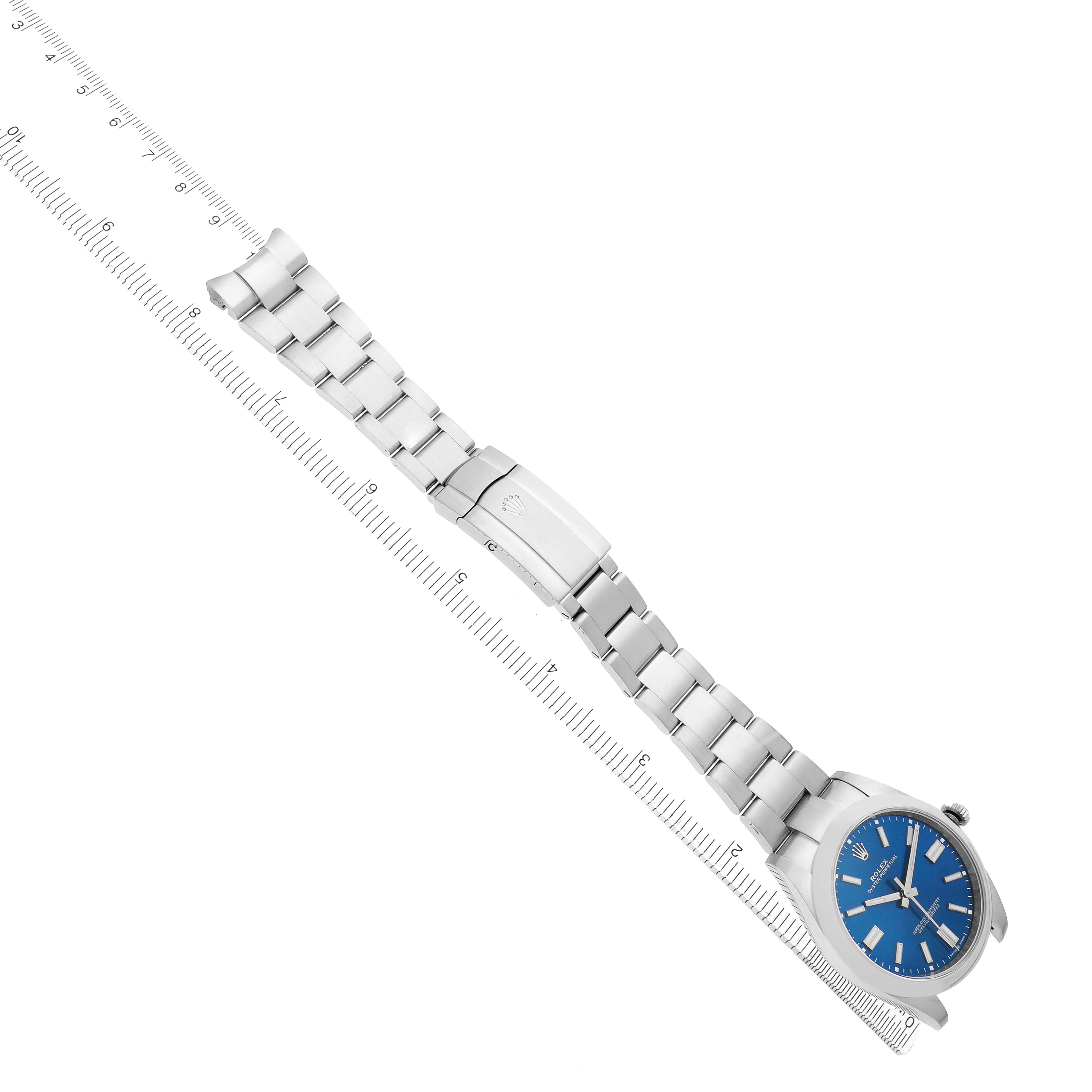 The Rolex Oyster Perpetual 124300 Men
s Stainless Steel Blue Dial watch is displayed flat, showcasing the bracelet and clasp, alongside a ruler for scale.