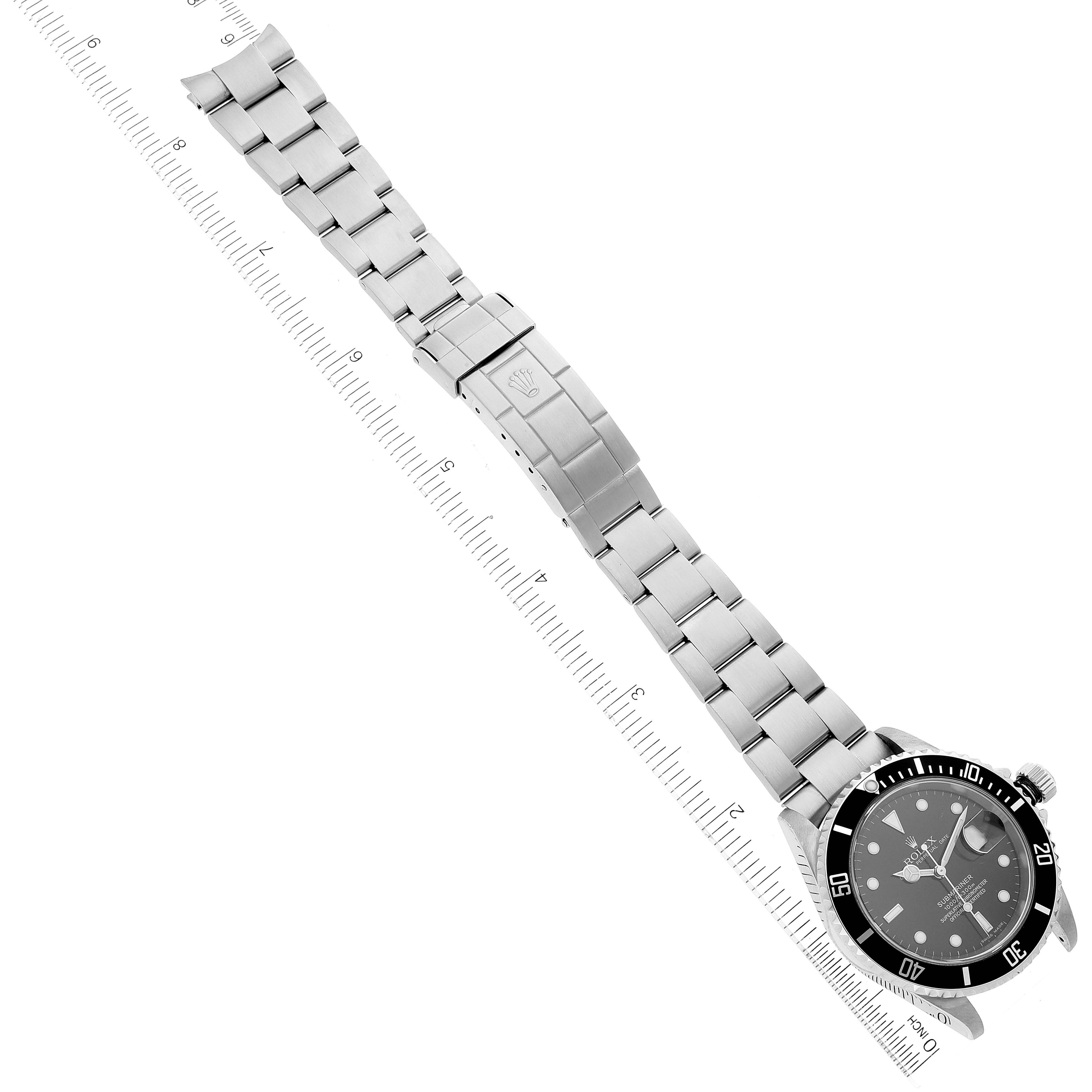 The image shows a top-down view of a Rolex Submariner 16610 Men
s Stainless Steel Black Dial 16610 Men
s Stainless Steel Black Dial watch, including its stainless steel bracelet and clasp, placed next to a ruler for scale.