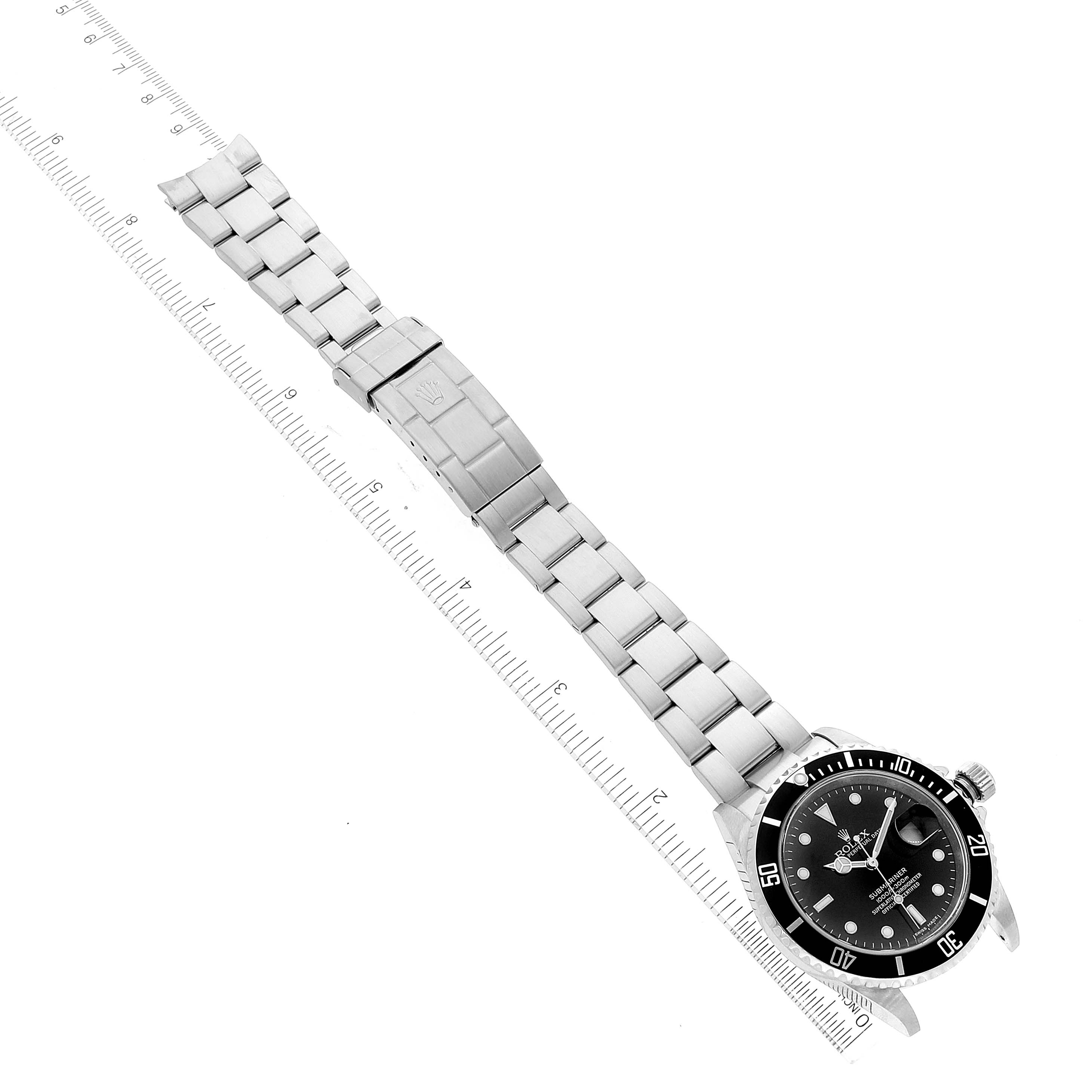 The image shows an angled, top view of a Rolex Submariner 16610 Men
s Stainless Steel Black Dial 16610 Men
s Stainless Steel Black Dial watch, displaying its bracelet, clasp, and face next to a ruler.