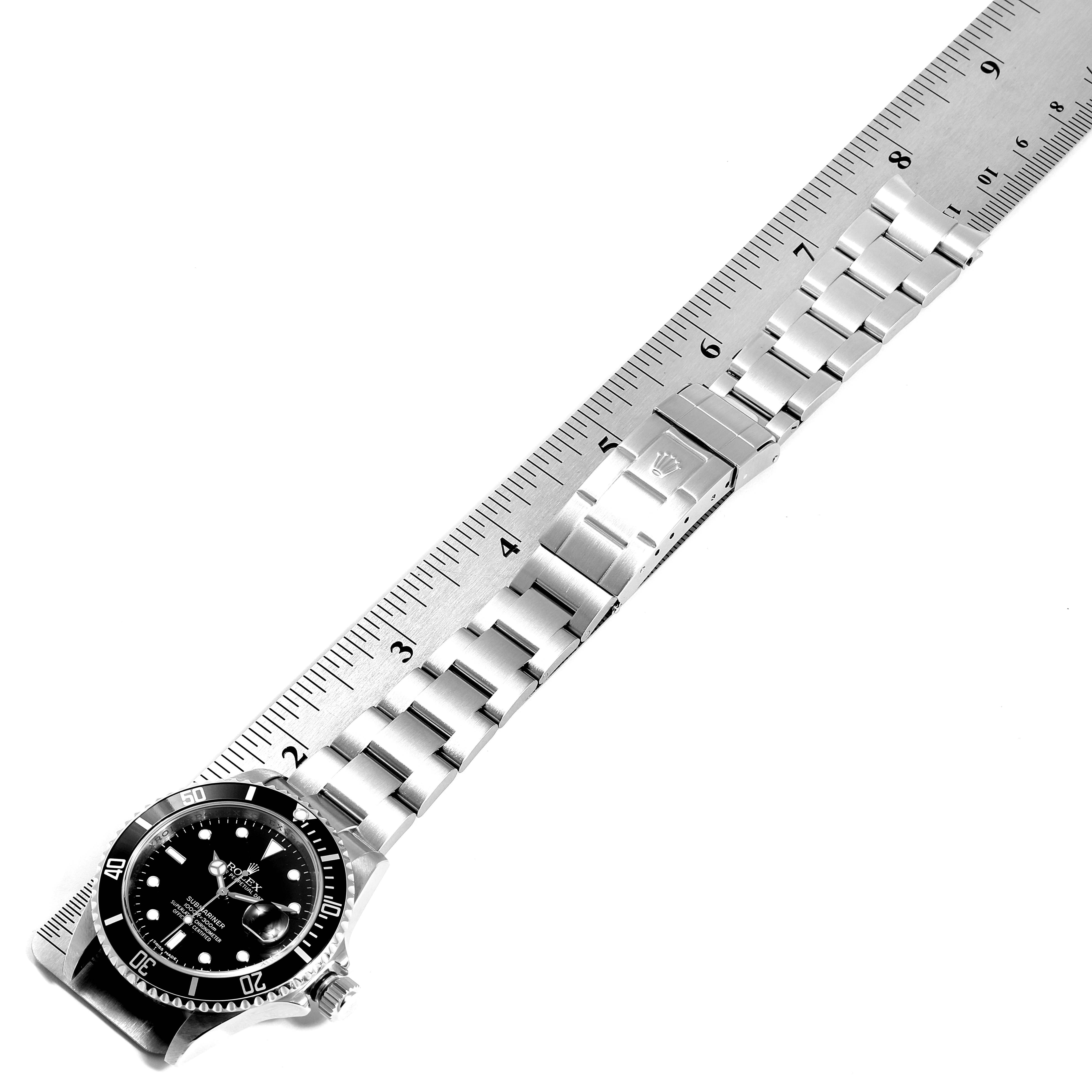The image shows a top-down view of a Rolex Submariner 16610 Men
s Stainless Steel Black Dial 16610 Men
s Stainless Steel Black Dial watch with its face, bezel, and full bracelet next to a ruler for scale.
