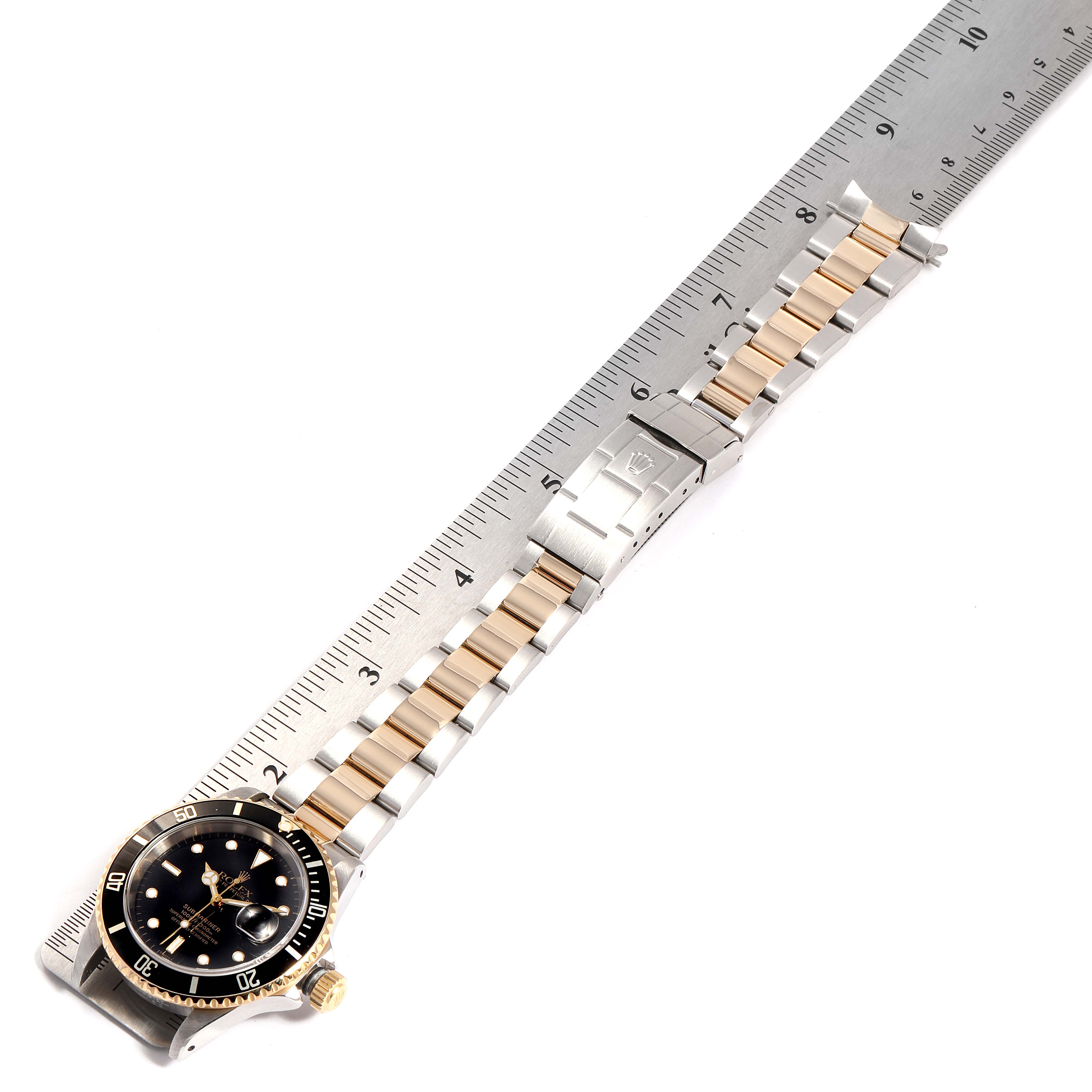 The image shows a Rolex Submariner 16613 Men's Steel and Gold (two tone) Black Dial 16613 Men's Steel and Gold (two tone) Black Dial watch with a metal and gold bracelet, displayed alongside a ruler for scale.