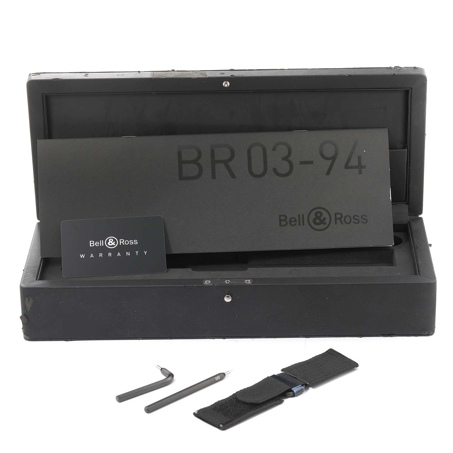 This image shows the open box of a Bell 
Ross Instruments BR03-90 Men
s Steel and Gold (two tone) Silver Dial BR03-90 Men
s Steel and Gold (two tone) Silver Dial BR03-94, warranty card, strap tool, and a nylon strap.