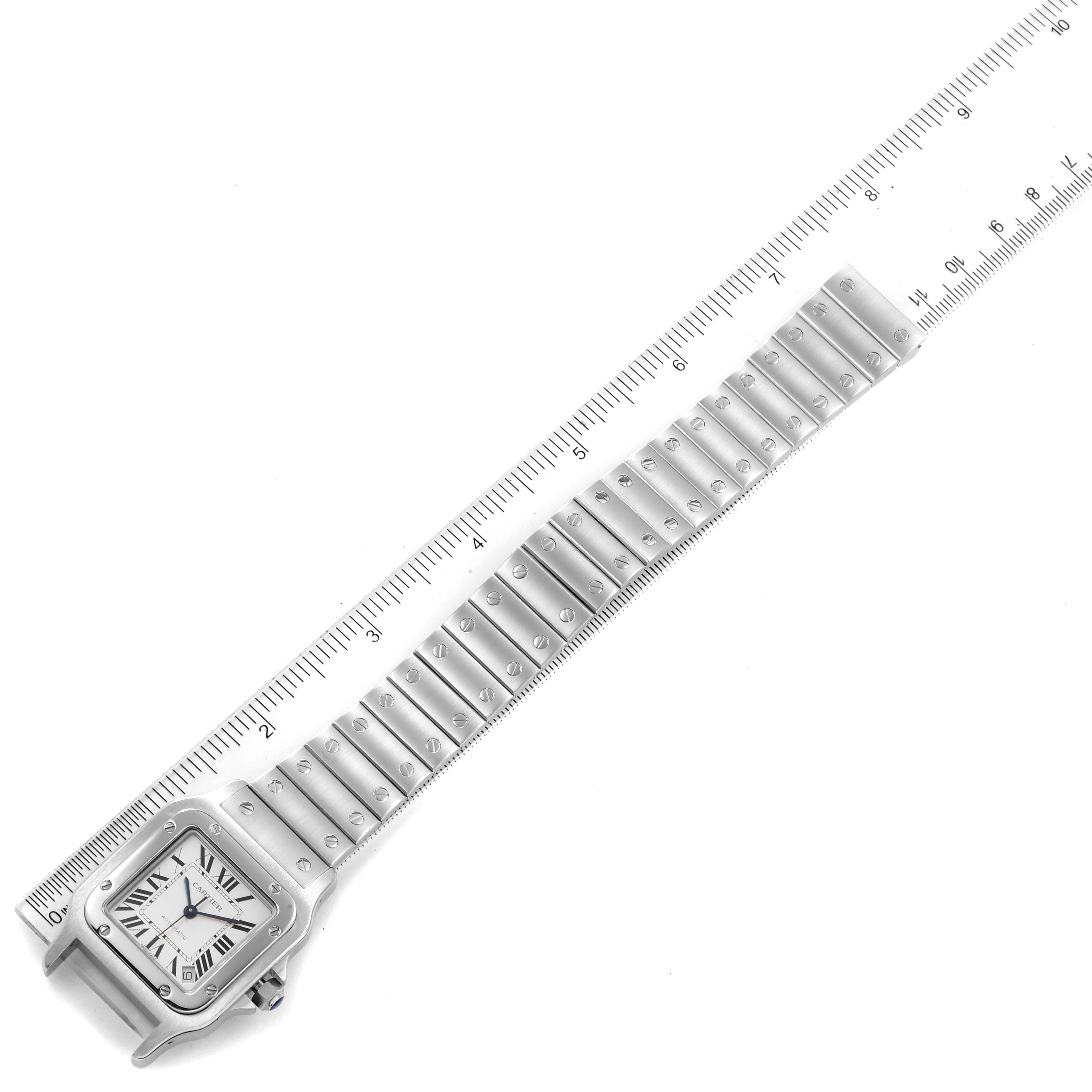 The image shows a Cartier Santos model W20098D6 men's watch viewed from above, highlighting the square face and stainless steel bracelet against a ruler background.