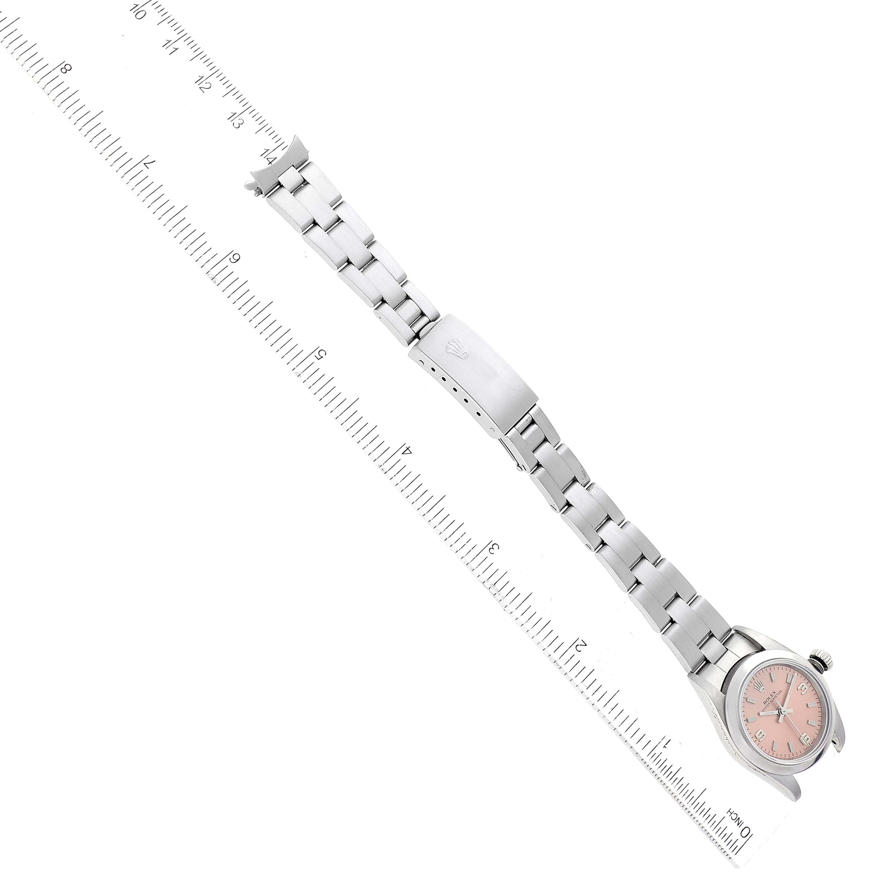 The image shows the Rolex Oyster Perpetual 76080 Women's Stainless Steel Pink Dial 76080 Women's Stainless Steel Pink Dial watch from an overhead angle, highlighting its bracelet and clasp beside a ruler.