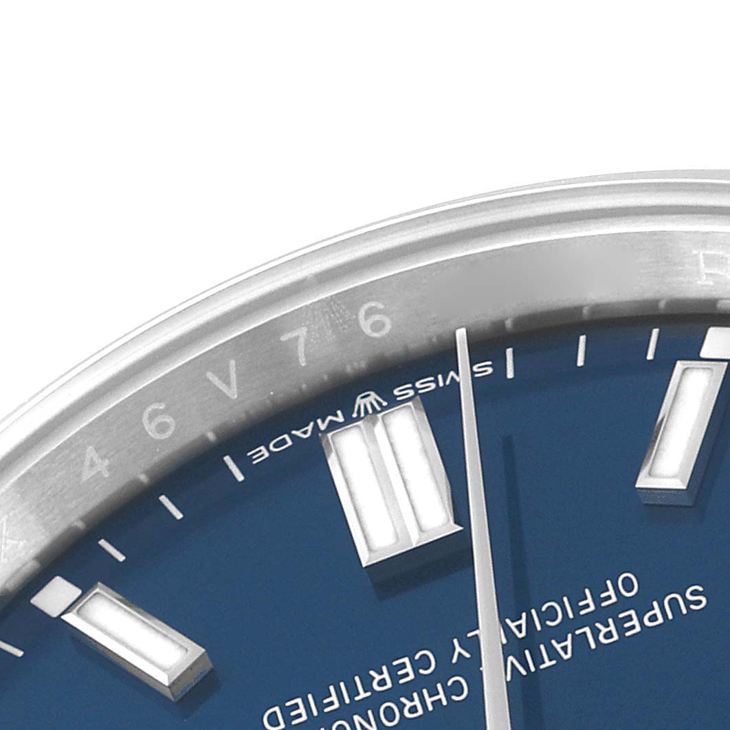 The image shows a close-up of the upper right section of the dial and bezel of a Rolex Oyster Perpetual 126000 Men
s Stainless Steel Blue Dial 126000 Men
s Stainless Steel Blue Dial watch, featuring indices and text.