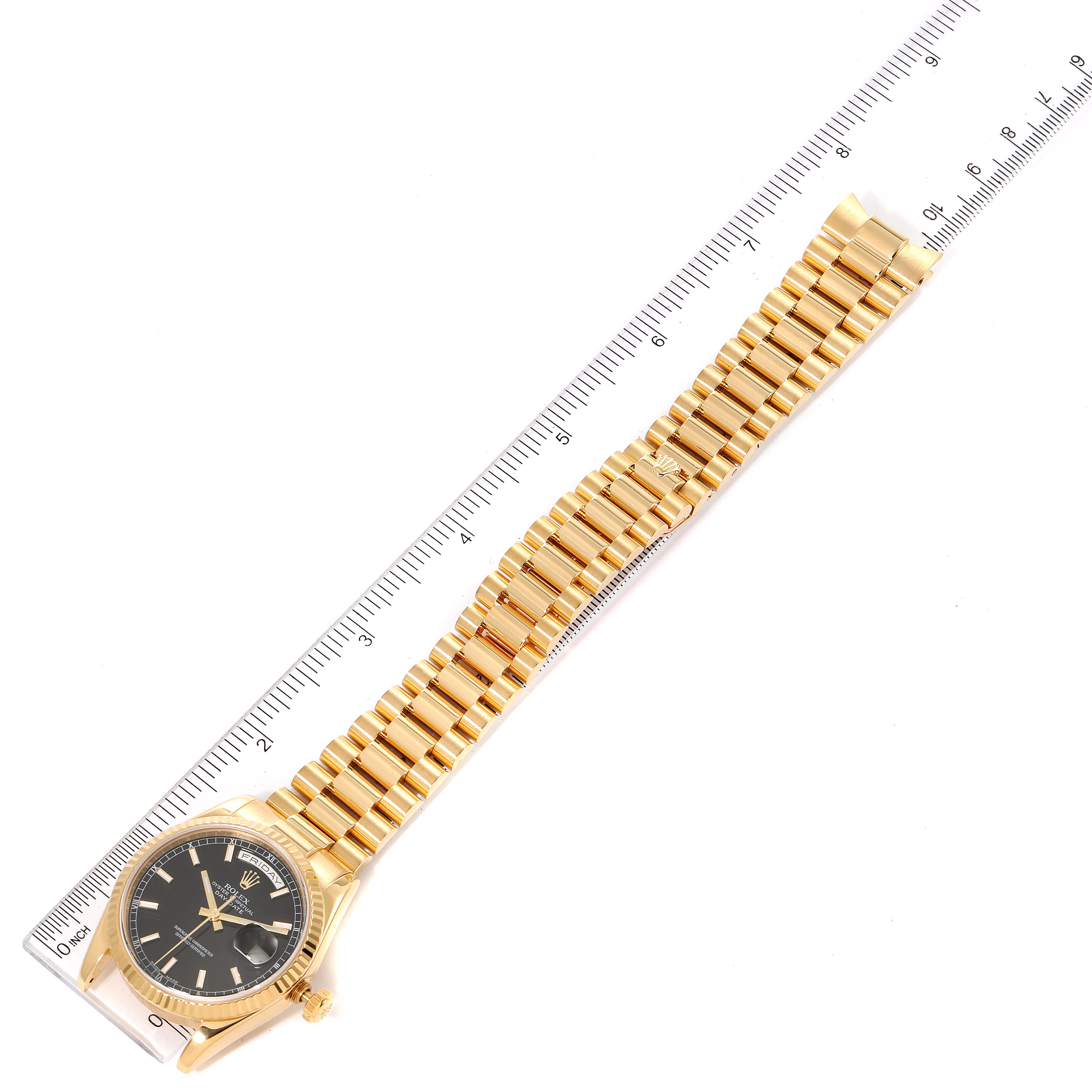 The image shows a Rolex President 118238 Men
s Yellow Gold Black Dial 118238 Men
s Yellow Gold Black Dial model watch laid flat with its gold bracelet and black dial face visible, alongside a ruler for scale.