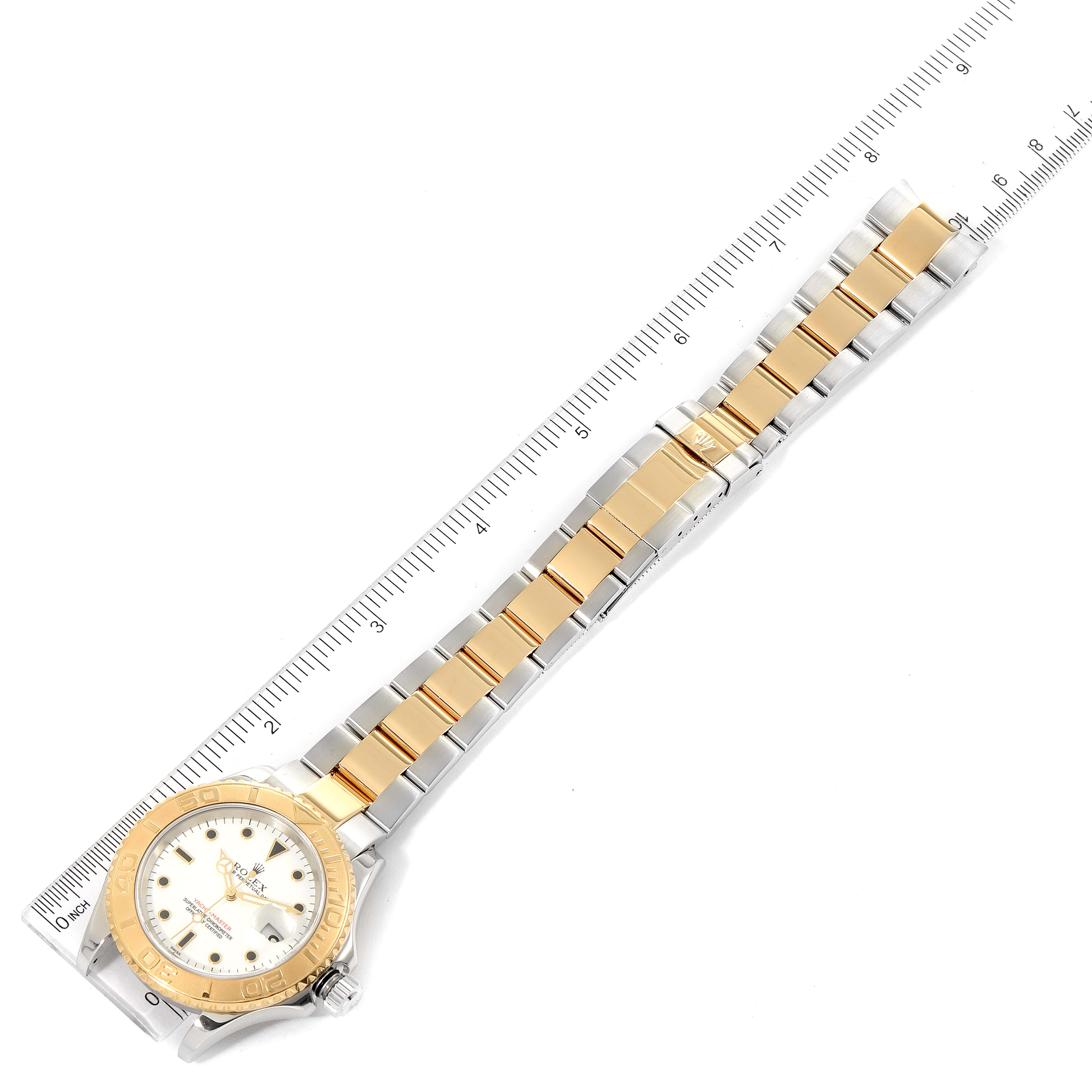 The Yacht-Master Rolex watch is shown flat with its gold and silver bracelet and face visible, aligned next to a ruler.