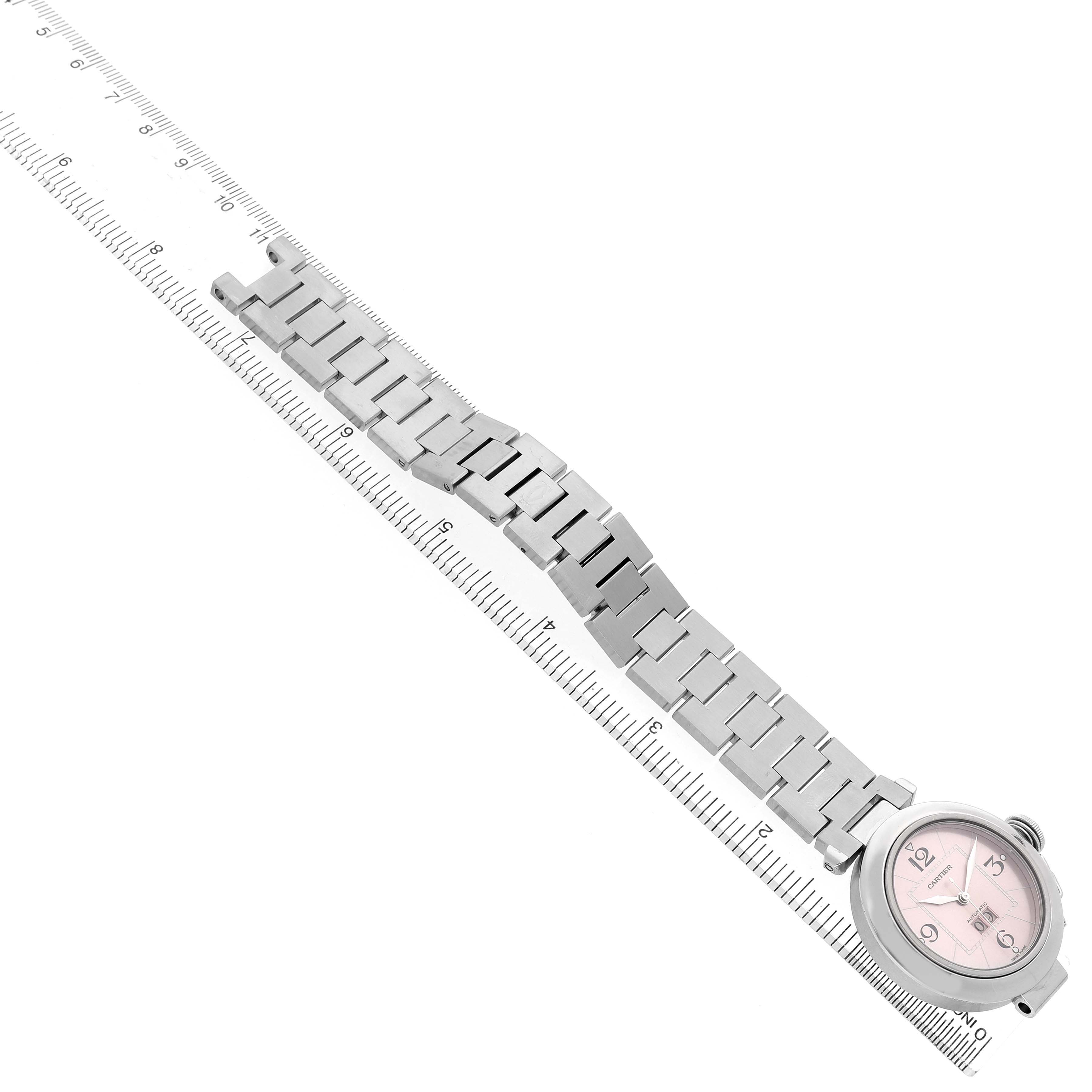 The Cartier Pasha W31058M7 Women's Stainless Steel Pink Dial watch is shown from the top, displaying the bracelet and round case, alongside a ruler for scale.