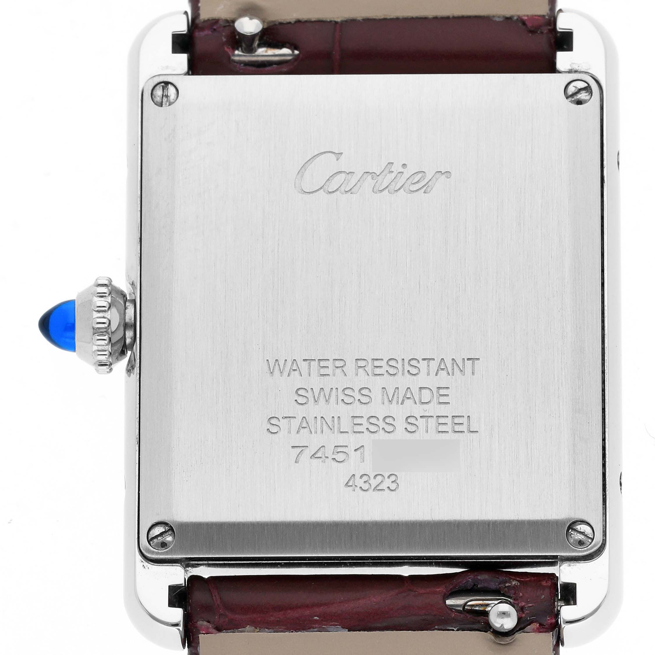 The image shows the back case of a Cartier Tank Must WSTA0054 Women's Stainless Steel Red Dial WSTA0054 Women's Stainless Steel Red Dial watch, displaying inscriptions and part of the strap and crown.