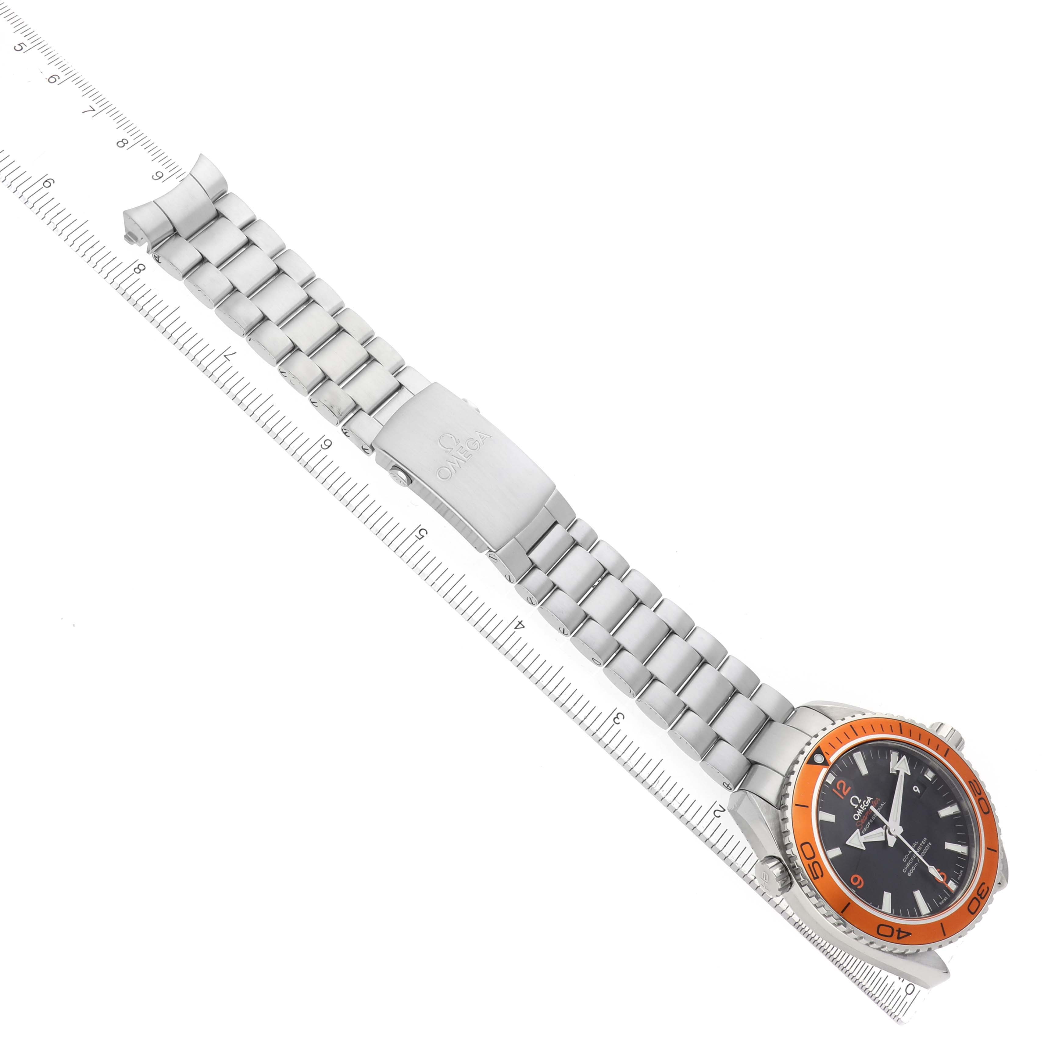 The Omega Planet Ocean 232.30.46.21.01.002 Men
s Stainless Steel Black Dial watch is shown diagonally, featuring the face, orange bezel, stainless steel bracelet, and clasp with a ruler.