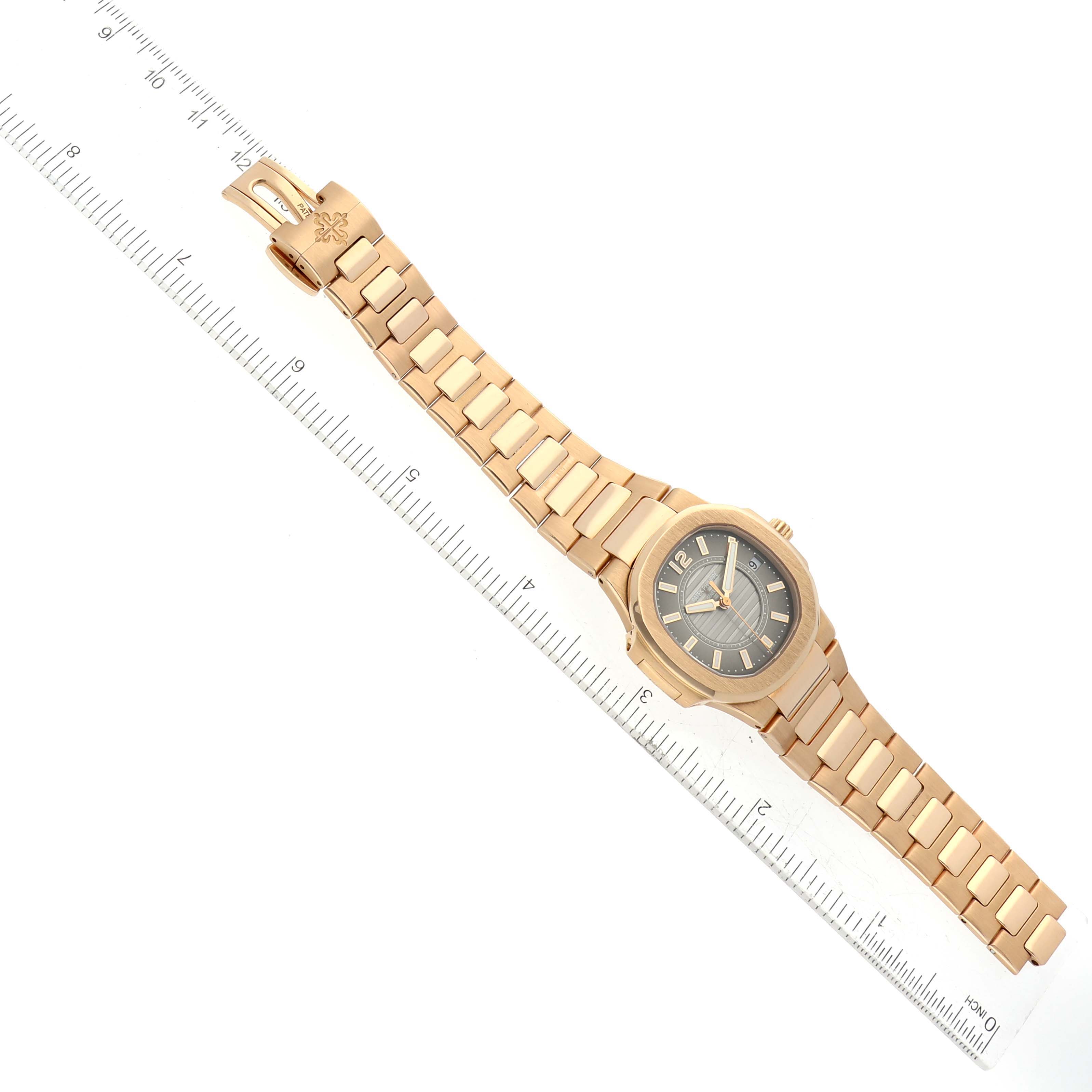 This image shows a Patek Philippe Nautilus 7011/1R Women's Rose Gold Grey Dial 7011/1R Women's Rose Gold Grey Dial watch laid flat next to a ruler, showcasing its entire band and face from a top-down angle.