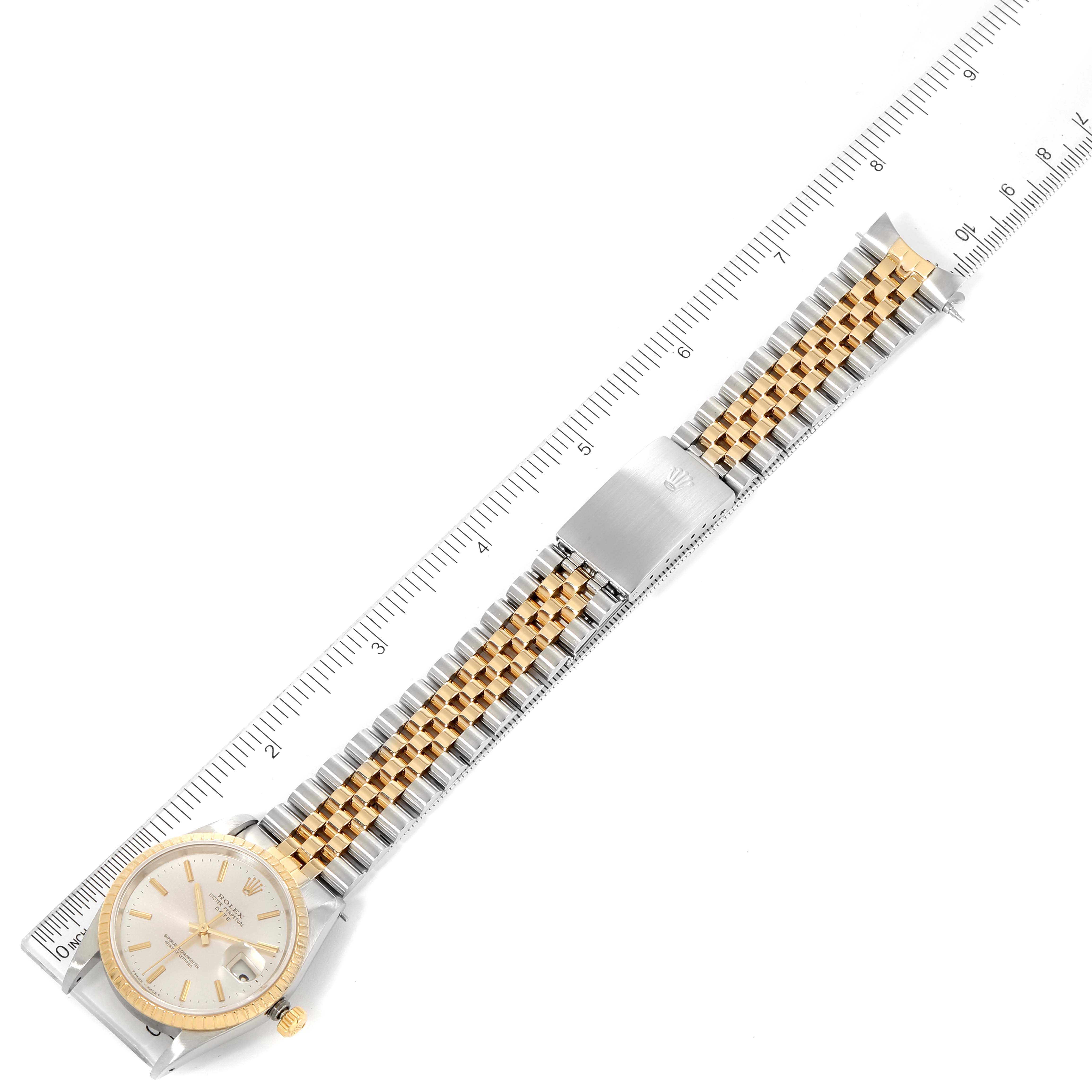 The image shows a Rolex Date 15223 Men's Steel and Gold (two tone) Silver Dial 15223 Men's Steel and Gold (two tone) Silver Dial model watch laid flat, including the dial, crown, and two-tone bracelet next to a ruler for measurement.
