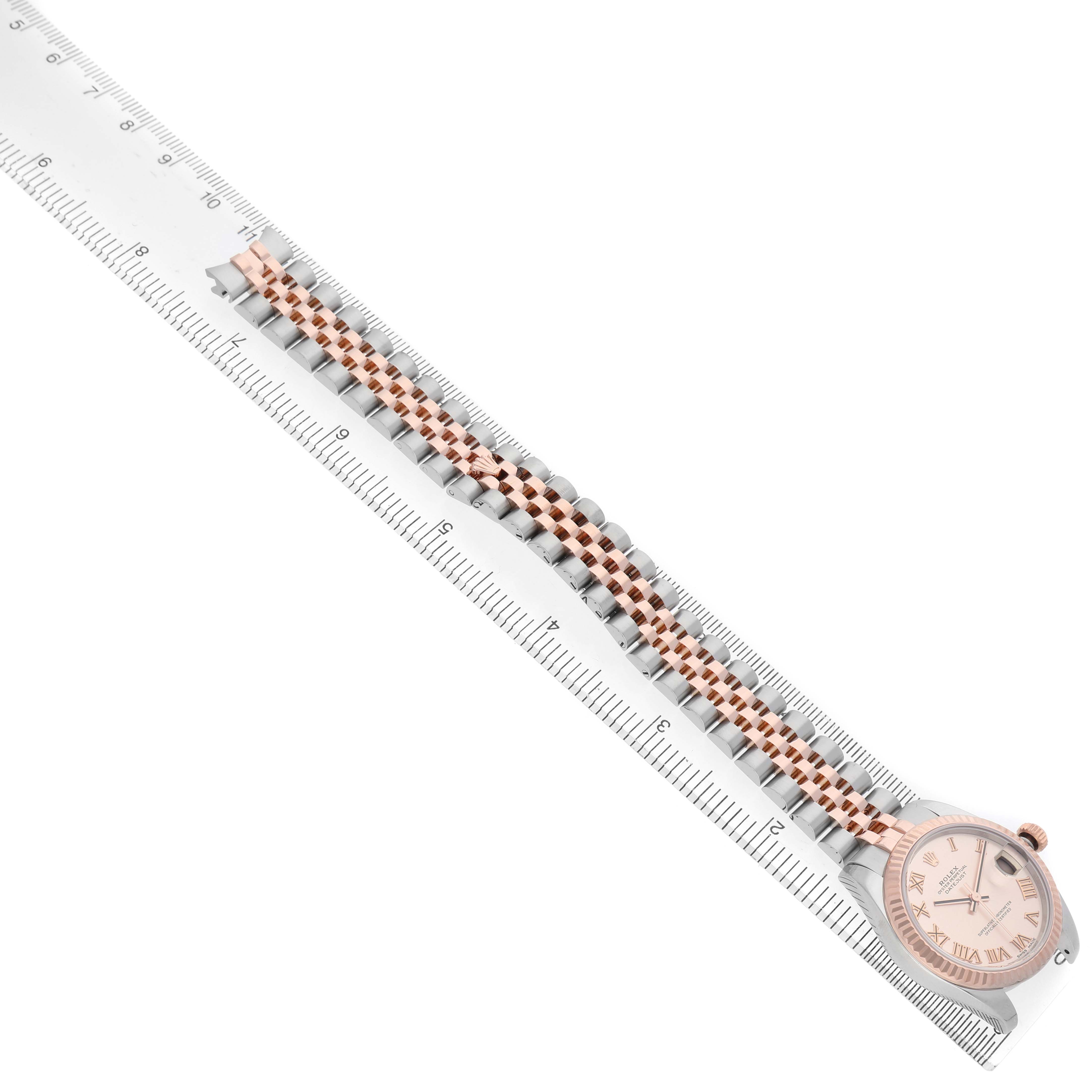 The Rolex Mid-Size 178271 Women's Steel and Gold (two tone) Pink Dial watch is displayed diagonally from a top view, showing the face, bezel, and bracelet aligned with a ruler.