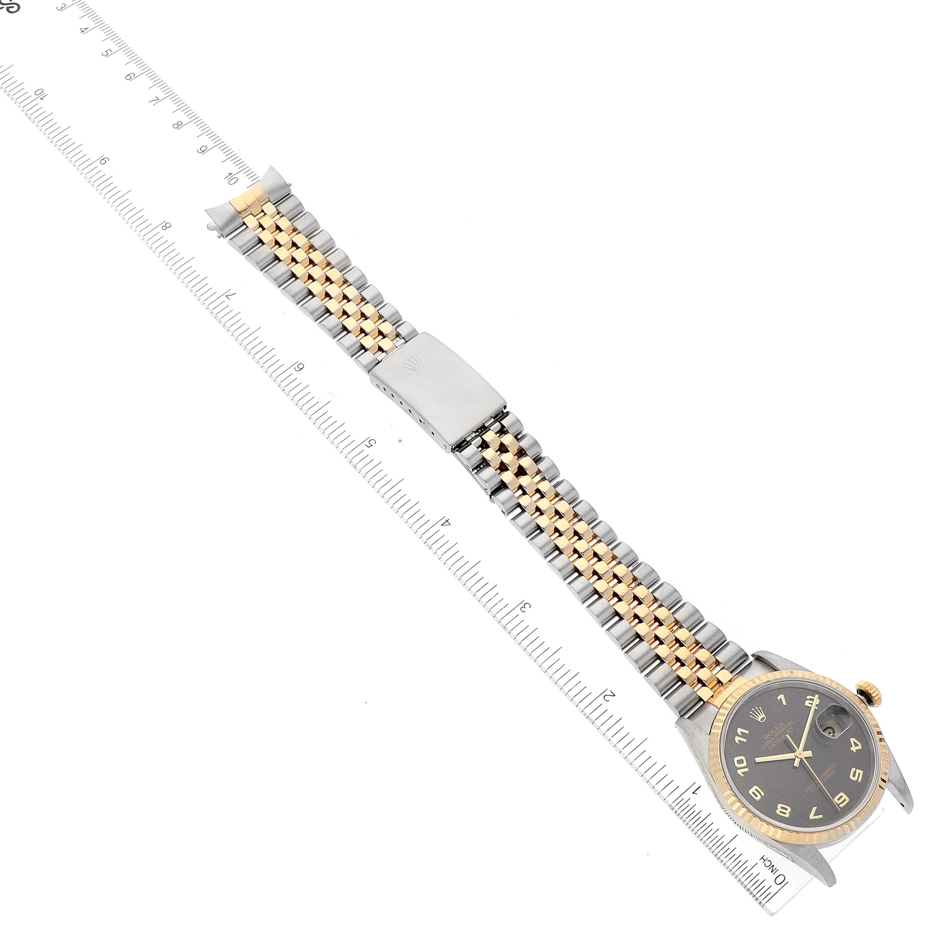 The image shows a top-down view of a Rolex Datejust 16233 Men's Steel and Gold (two tone) Black Dial 16233 Men's Steel and Gold (two tone) Black Dial watch, highlighting its face, bracelet, and clasp, alongside a measuring ruler.