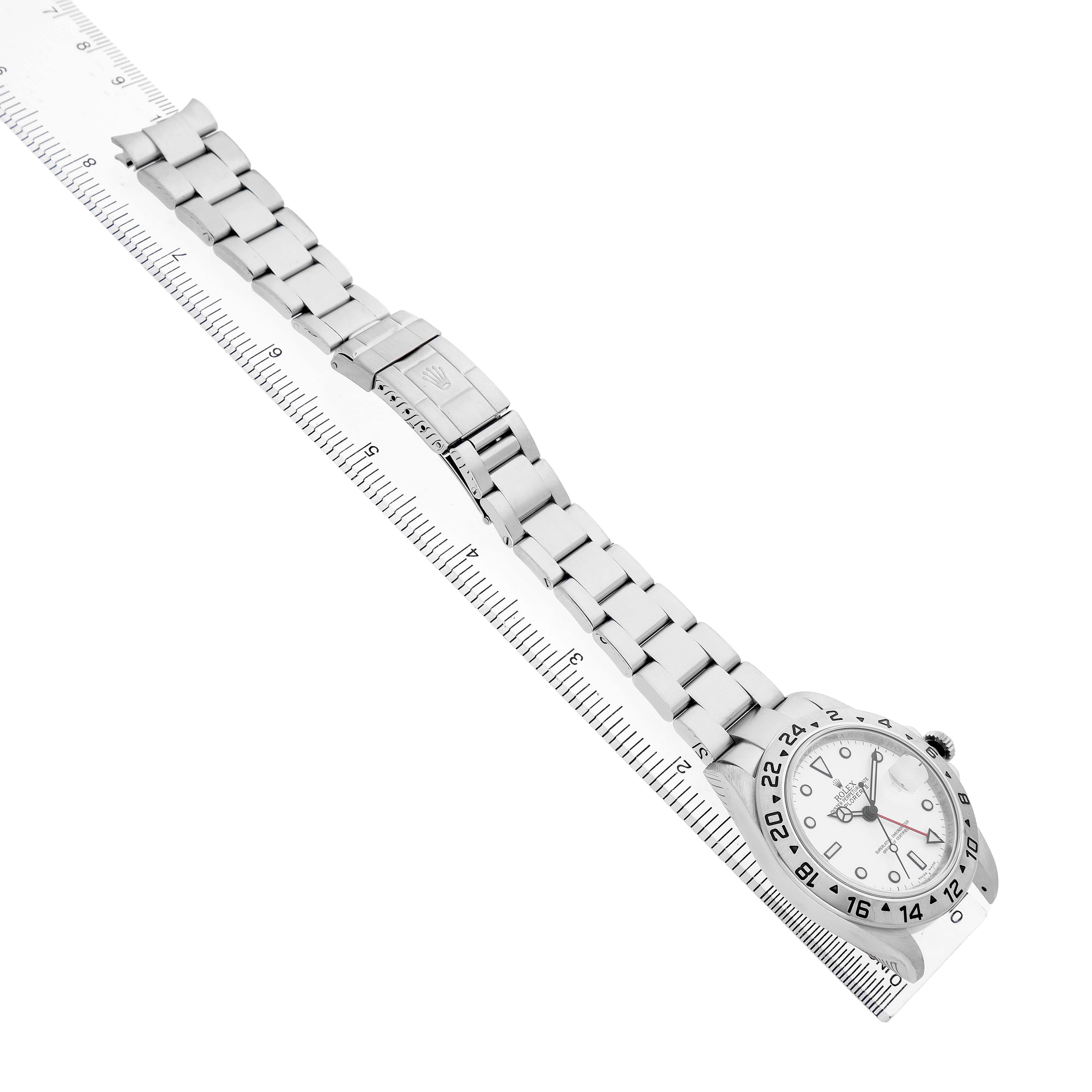 The Rolex Explorer 16570 Men's Stainless Steel White Dial watch is shown at an angle highlighting its bracelet, clasp, and face, placed alongside a ruler.