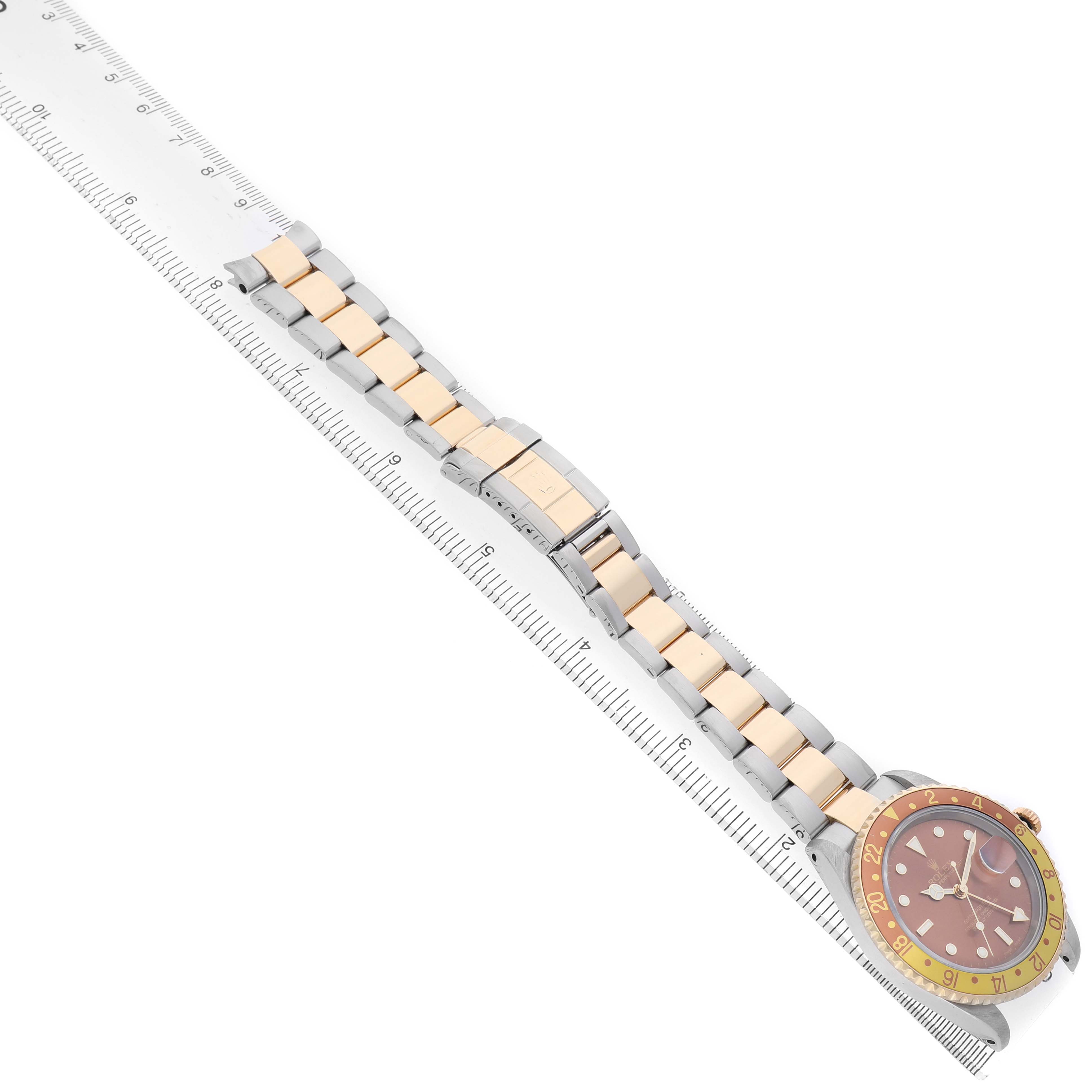The Rolex GMT-Master 16713 Men's Steel and Gold (two tone) Brown Dial watch is shown from a top angle, with its bracelet and ruler for scale.