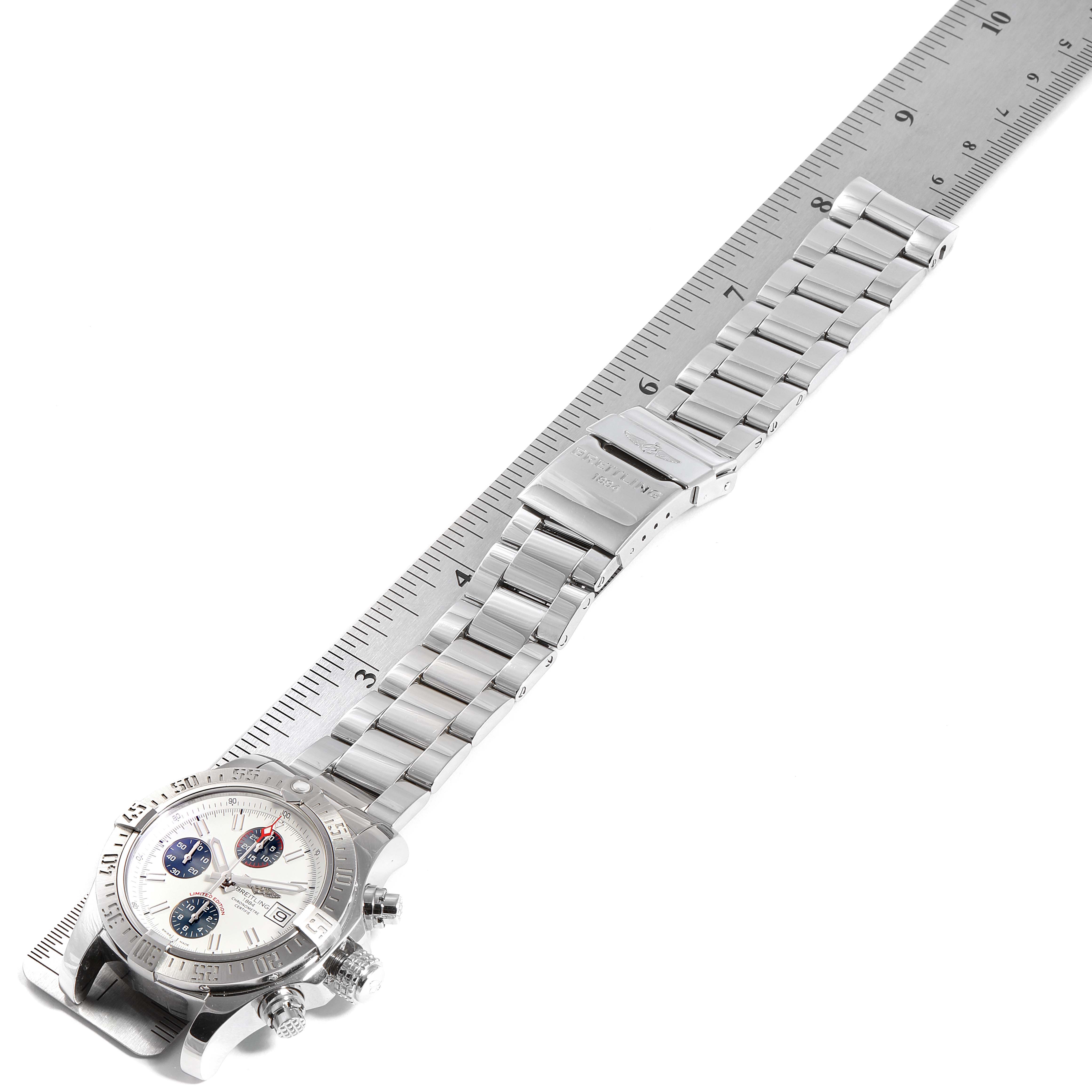 The image shows a side angle view of the Breitling Avenger A13381 Men's Stainless Steel White Dial A13381 Men's Stainless Steel White Dial watch, including its face, bezel, and metal bracelet laid against a ruler.