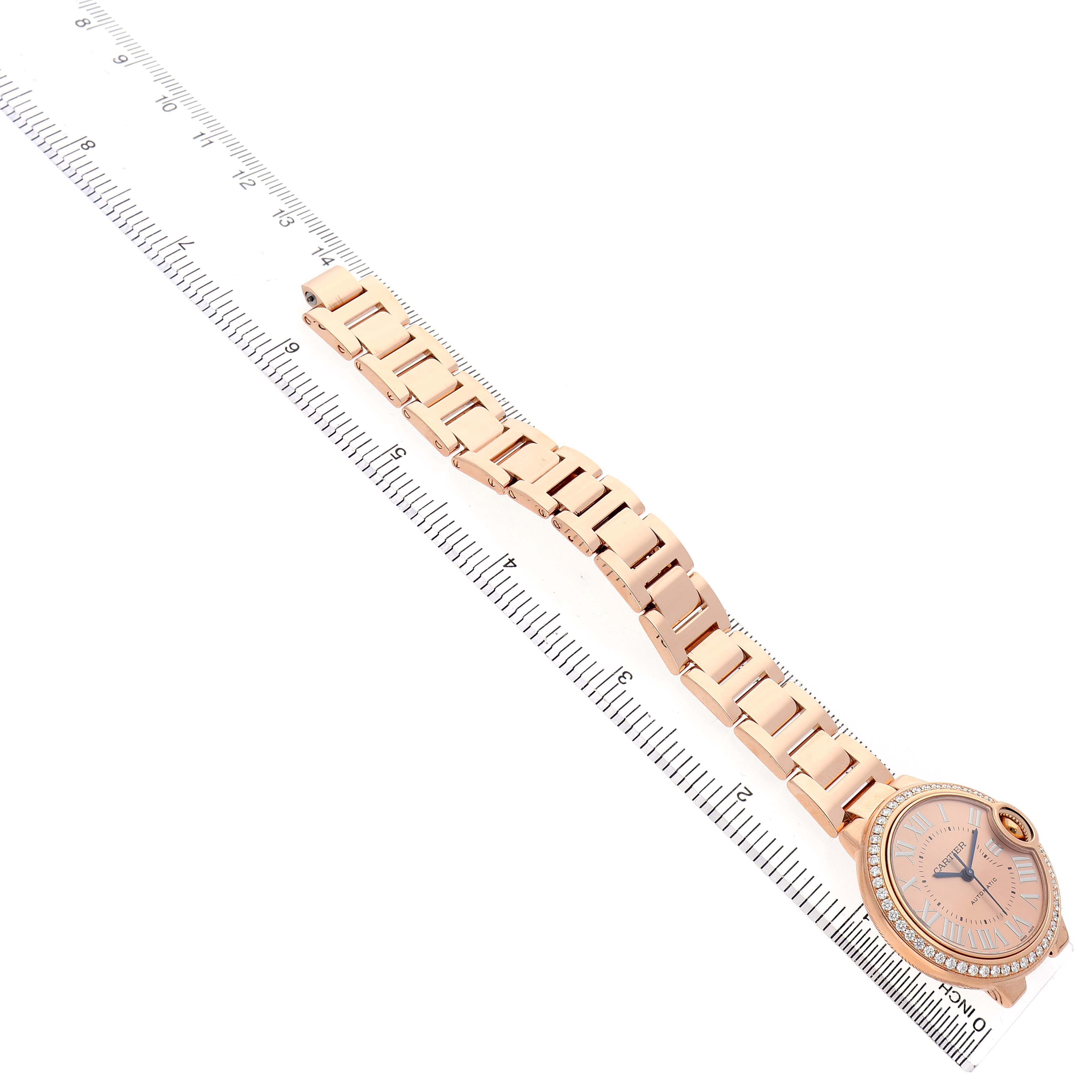 The image shows a Cartier Ballon Bleu WJBB0077 Women's Yellow Gold Pink Dial watch at an angled top view, highlighting the bracelet and face beside a ruler.