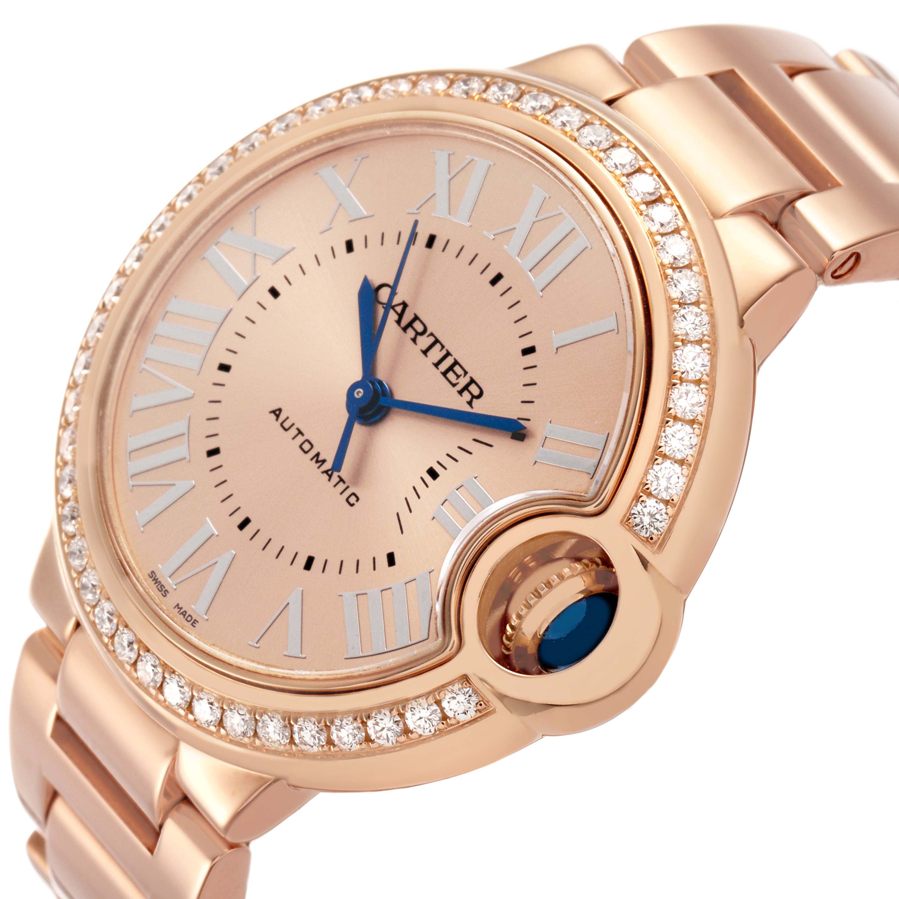 The Cartier Ballon Bleu WJBB0077 Women's Yellow Gold Pink Dial watch is shown at a three-quarter angle, highlighting the diamond bezel, blue hands, and cabochon crown.